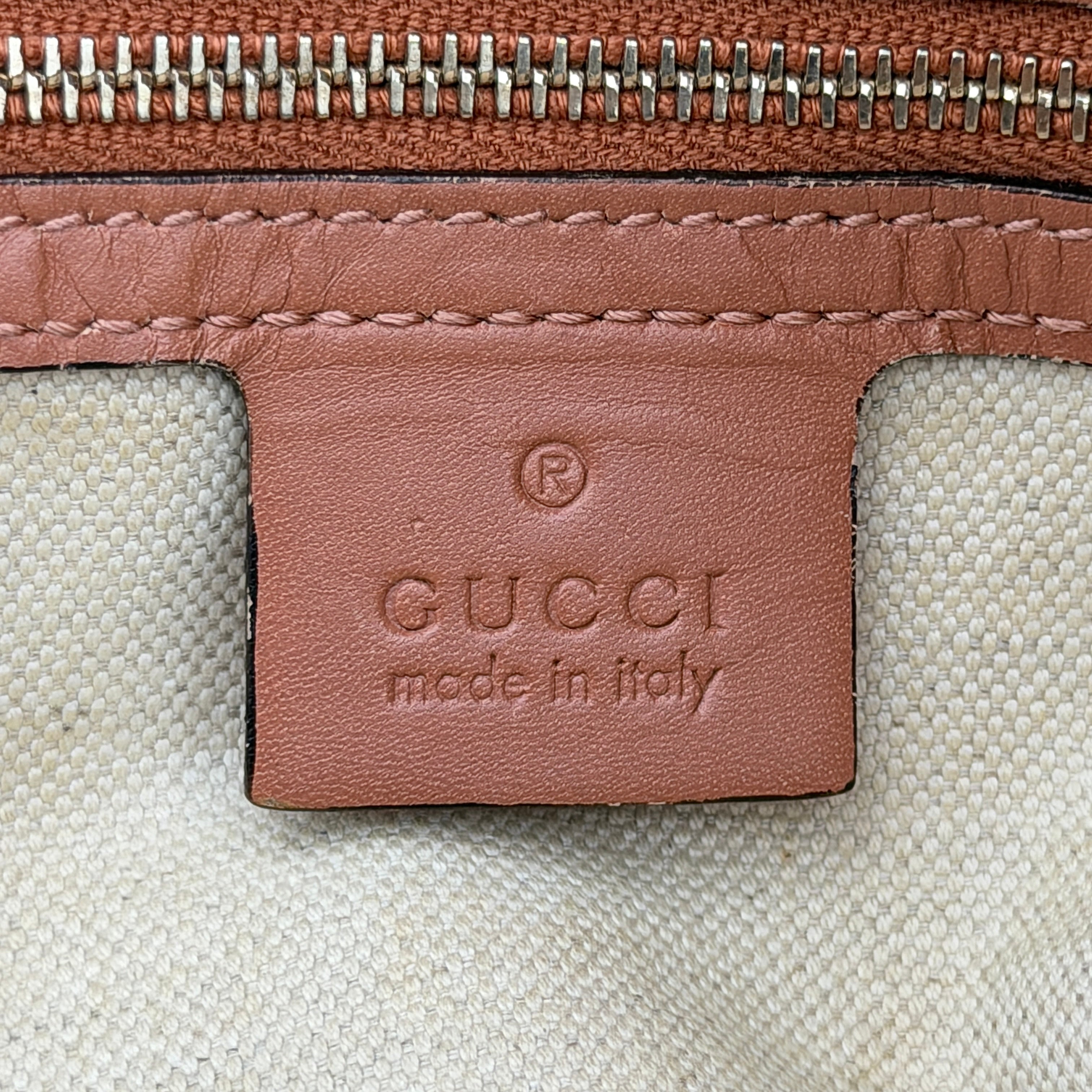 Gucci beige GG monogram shoulder bag with orange leather trim, heart bit charm, and detachable strap displayed on a white background.