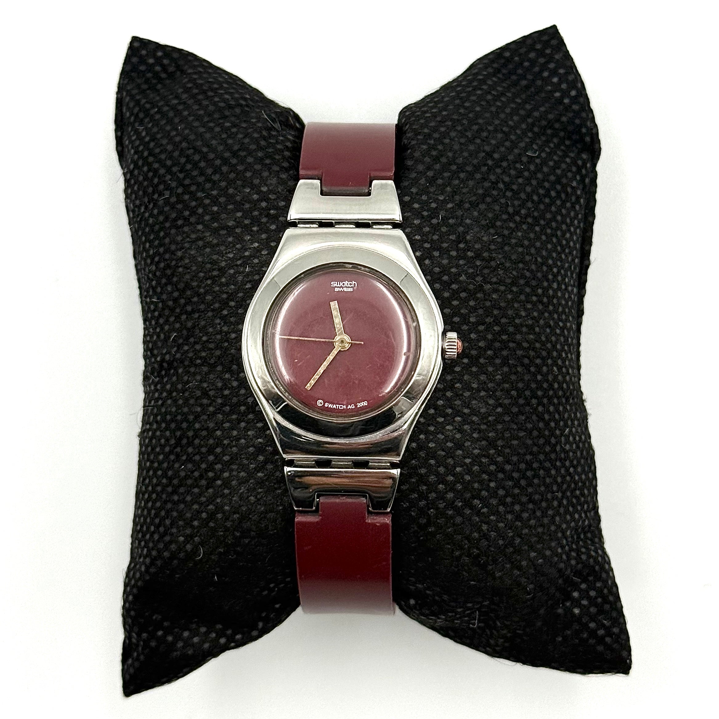 Swatch Irony Lady Angels Call watch in burgundy and silver, presented on a black cushion.