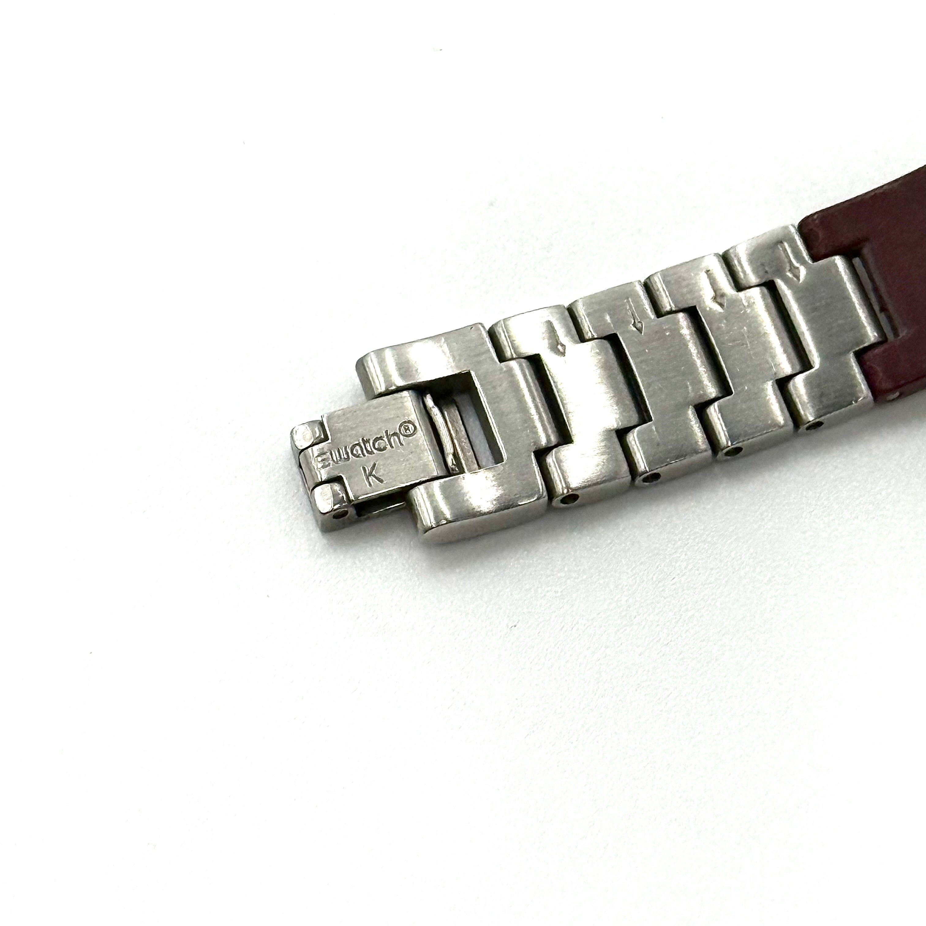 Swatch Irony Lady Angels Call watch in burgundy and silver, presented on a black cushion.