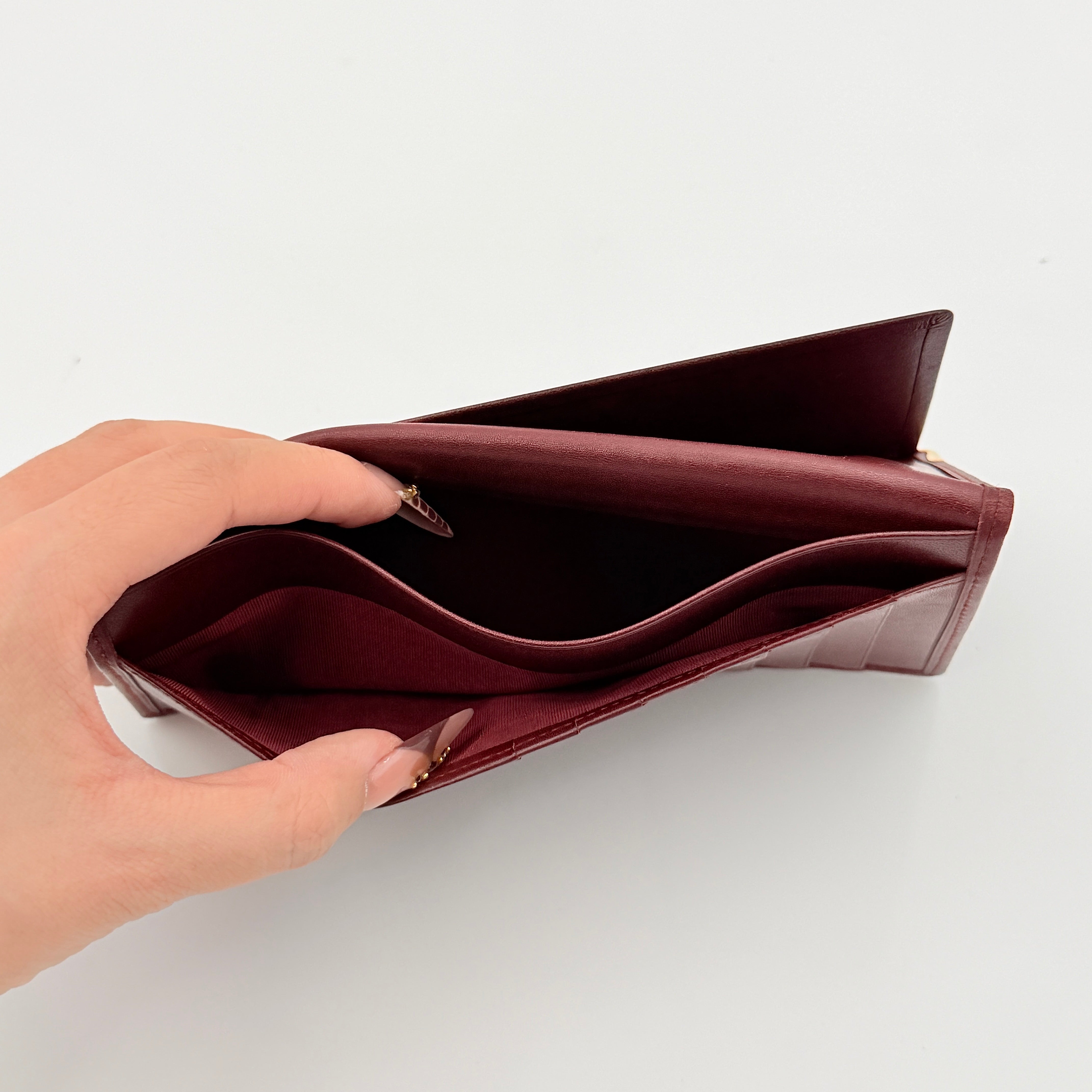 The Cartier Must de Cartier long bifold wallet in rich bordeaux calfskin with gold-tone corner accents and an embossed logo.