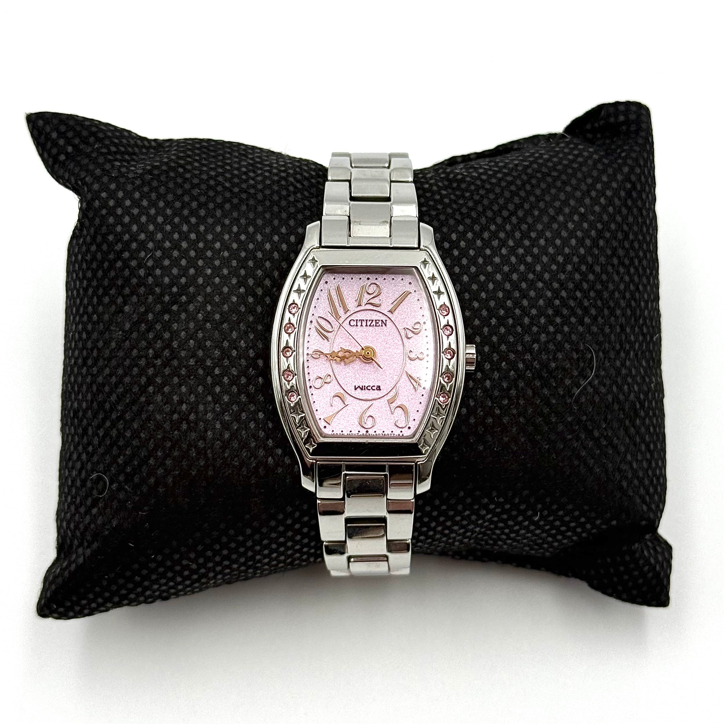 Citizen Wicca stainless steel watch with pink dial and star-detailed bezel shown on a black cushion.