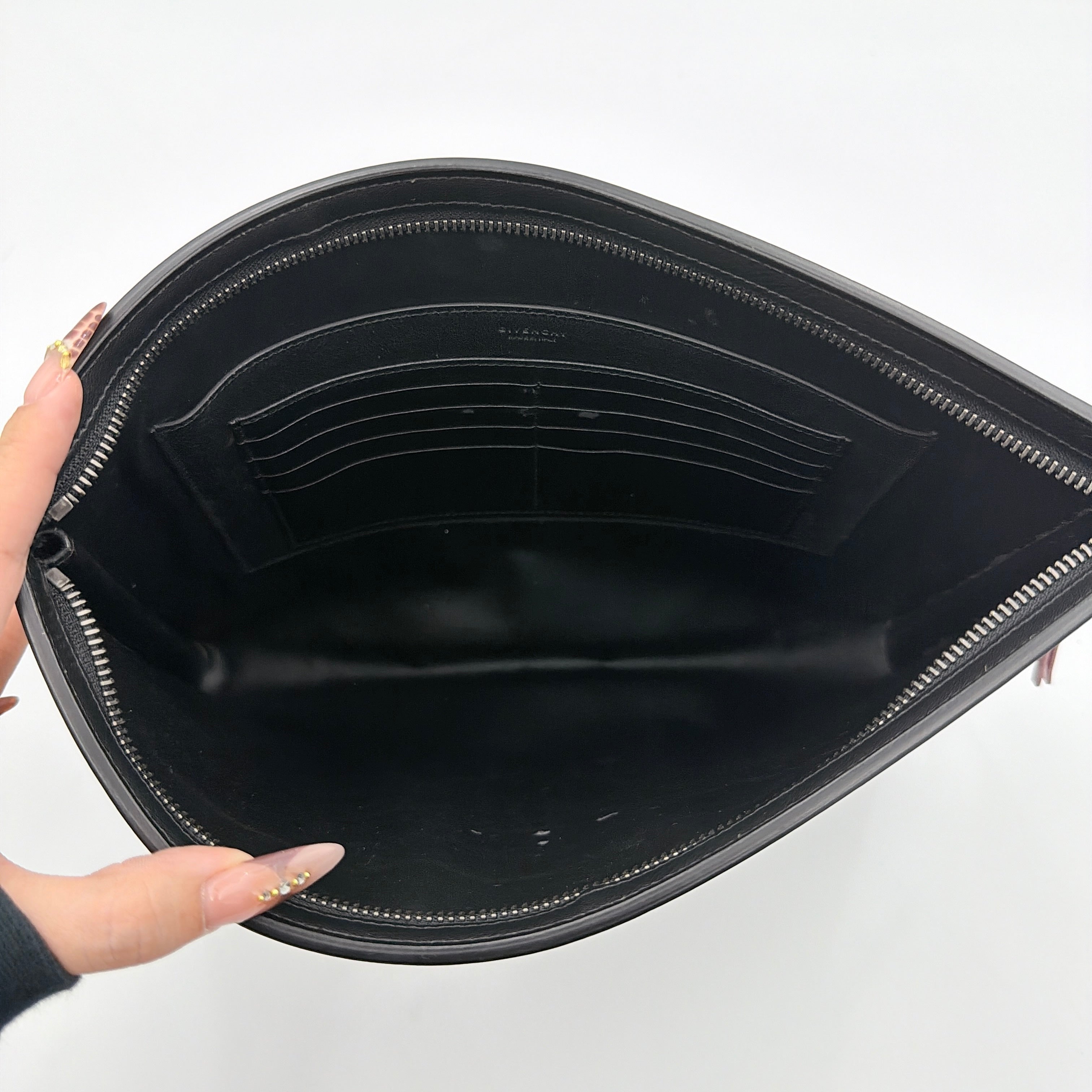 Front view of a Givenchy black leather clutch with bold white logo panel and red zip pull.