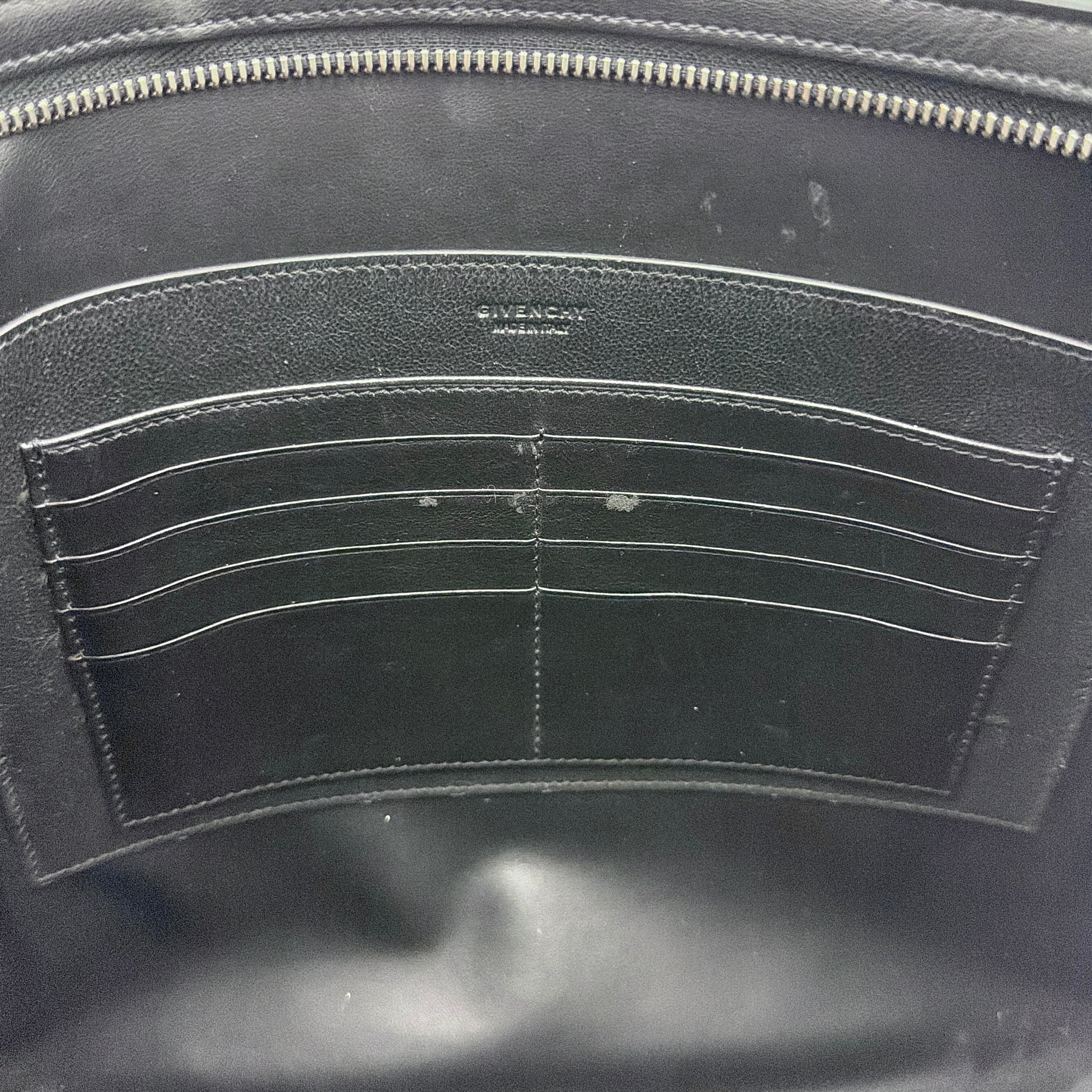 Front view of a Givenchy black leather clutch with bold white logo panel and red zip pull.