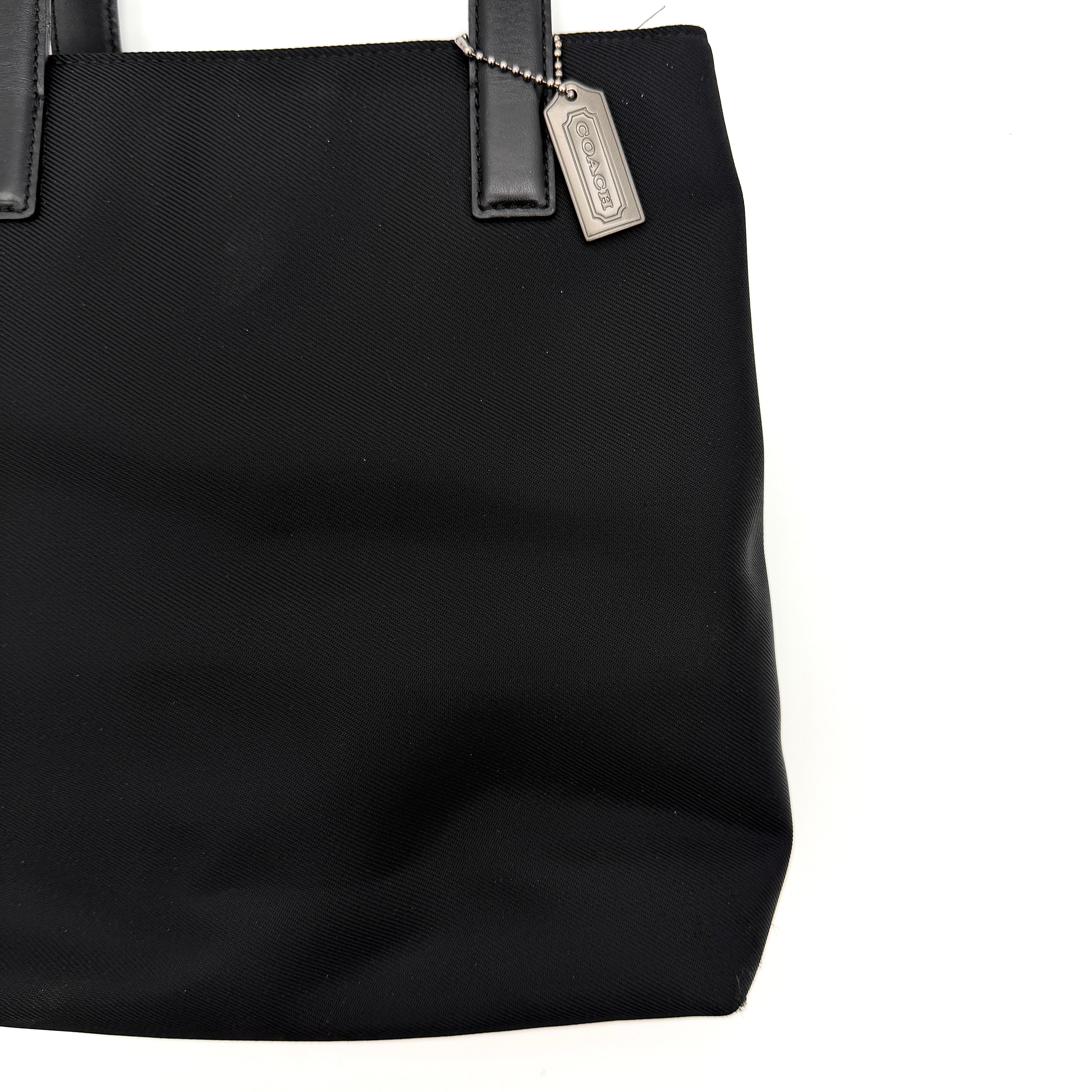 Coach Mercer Nylon Tote Bag in black with leather handles and silver Coach tag, photographed on a white background.
