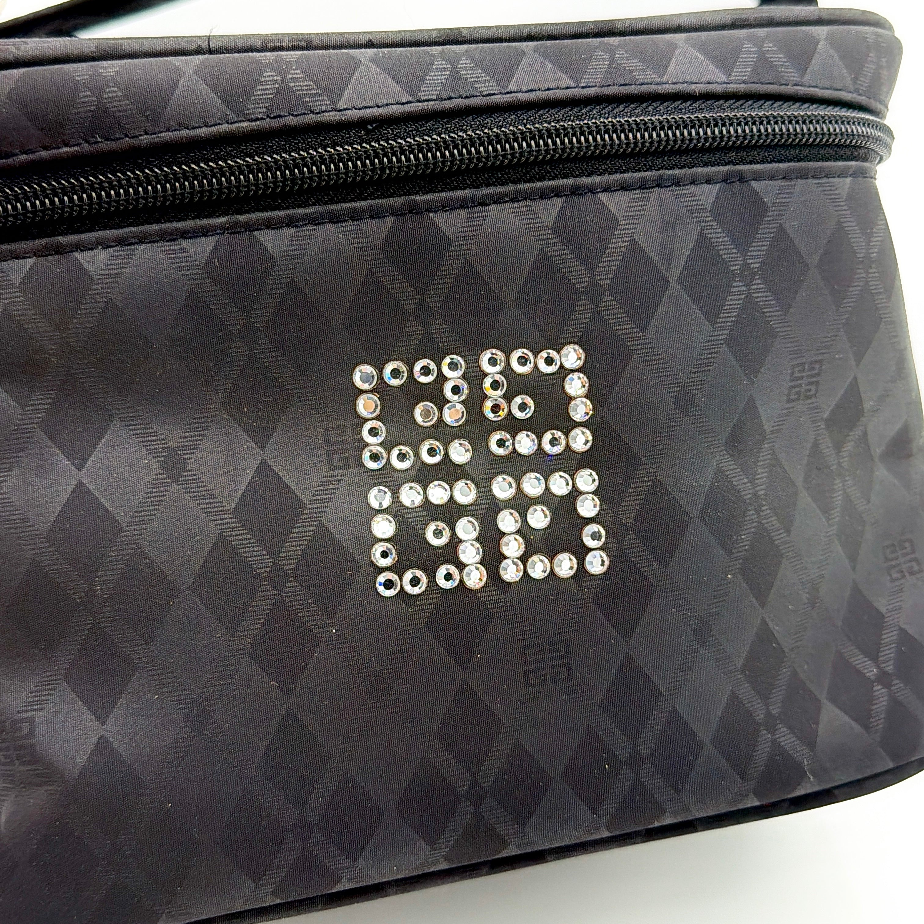 Givenchy vanity bag in black with rhinestone logo, geometric pattern, and top handle, shown from the front.