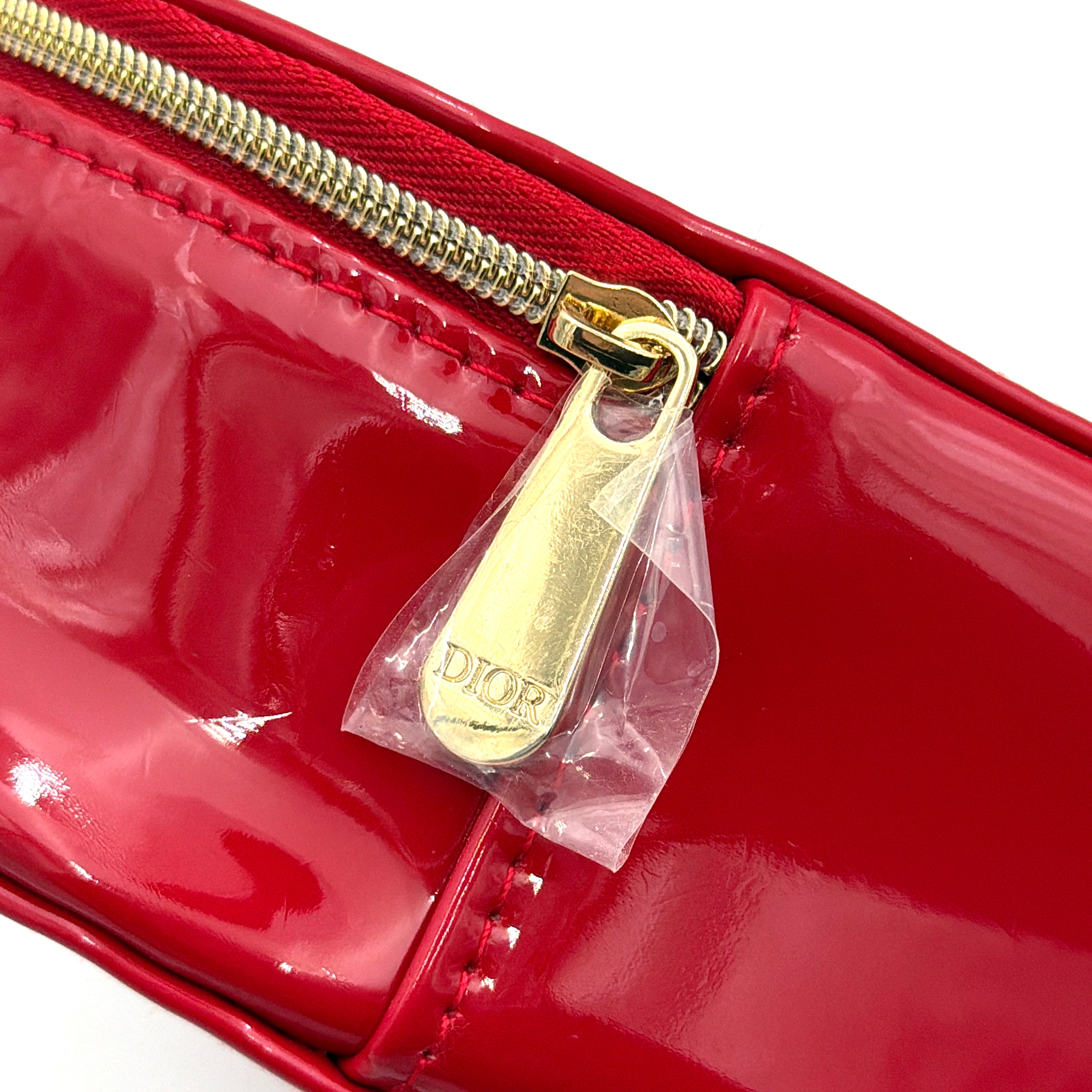 Christian Dior patent leather cosmetic pouch in glossy red with embossed DIOR logo and gold zip hardware.