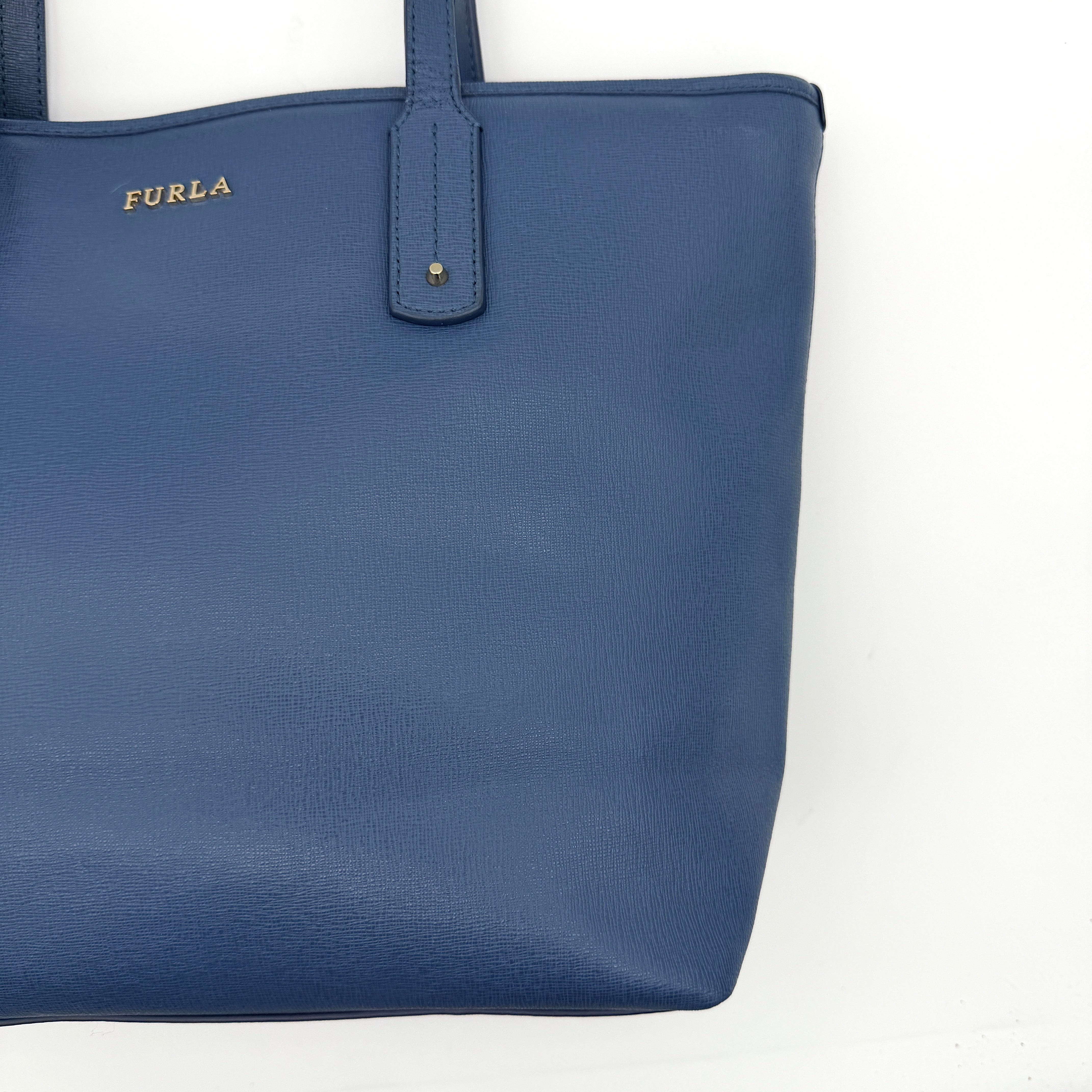 Furla New Daisy Tote Bag in blue leather with gold-tone logo charm and double handles, displayed against a white background