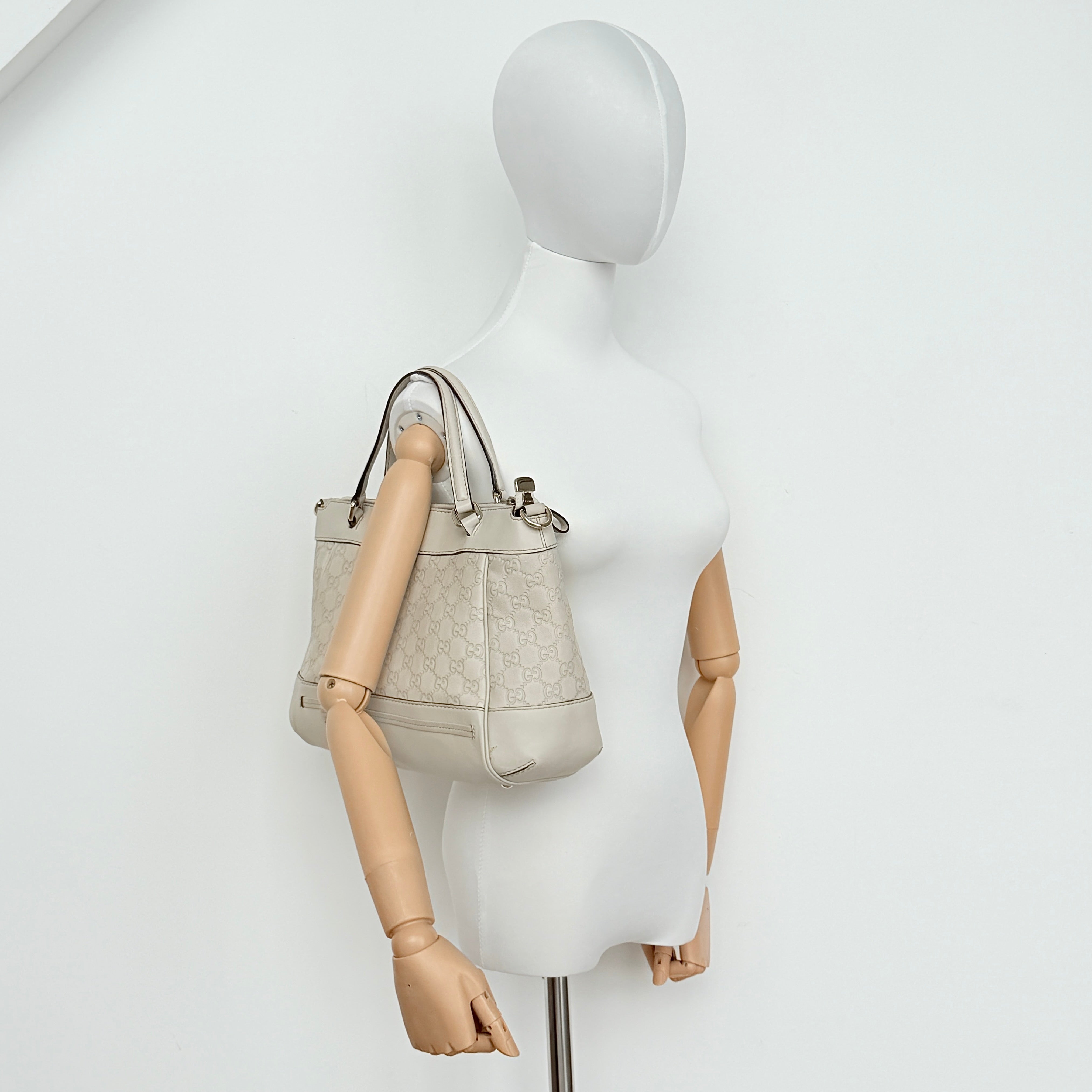 Gucci Mayfair Bow 2Way shoulder bag in cream GG monogram leather with dual handles and detachable strap, styled against a neutral backdrop.
