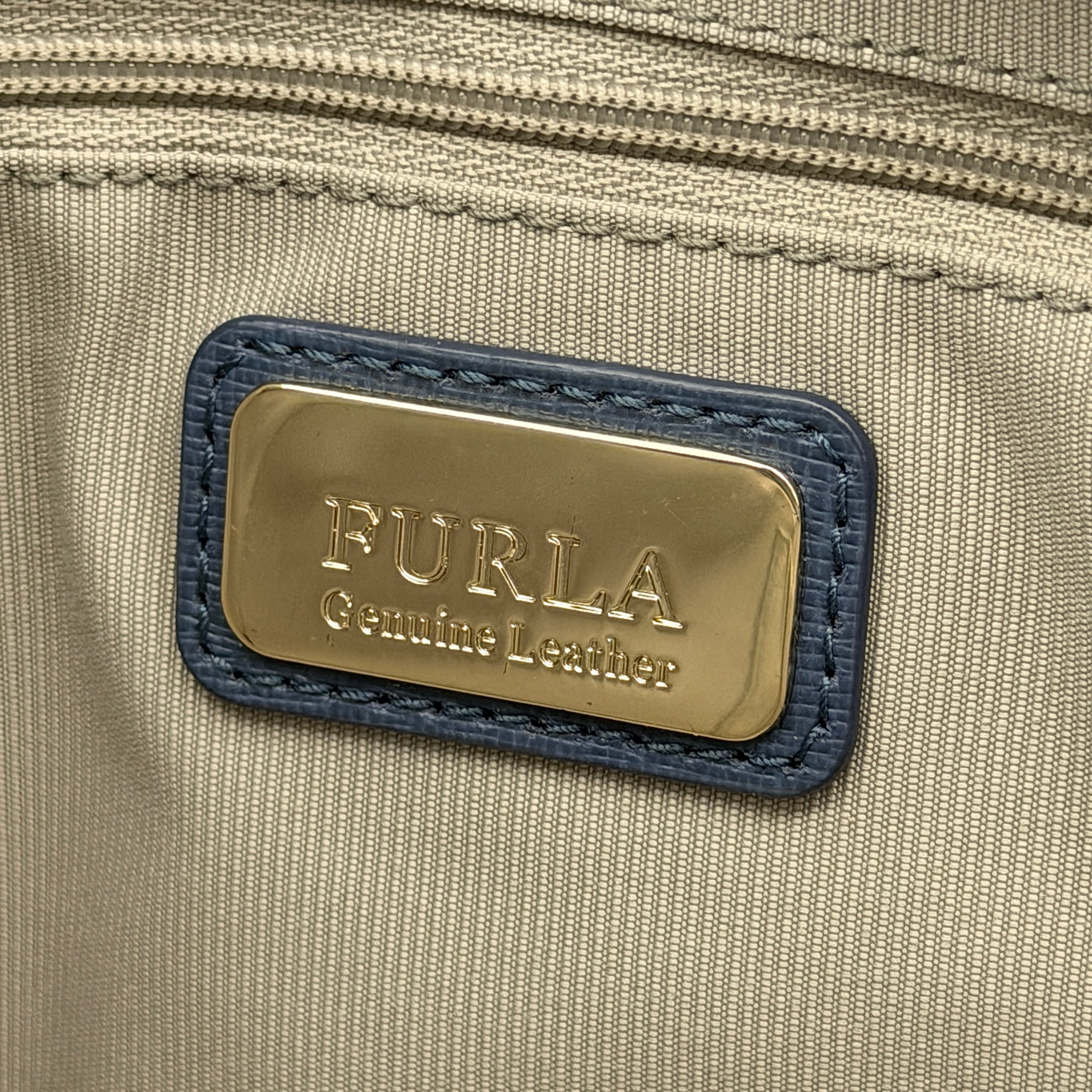 Furla New Daisy Tote Bag in blue leather with gold-tone logo charm and double handles, displayed against a white background