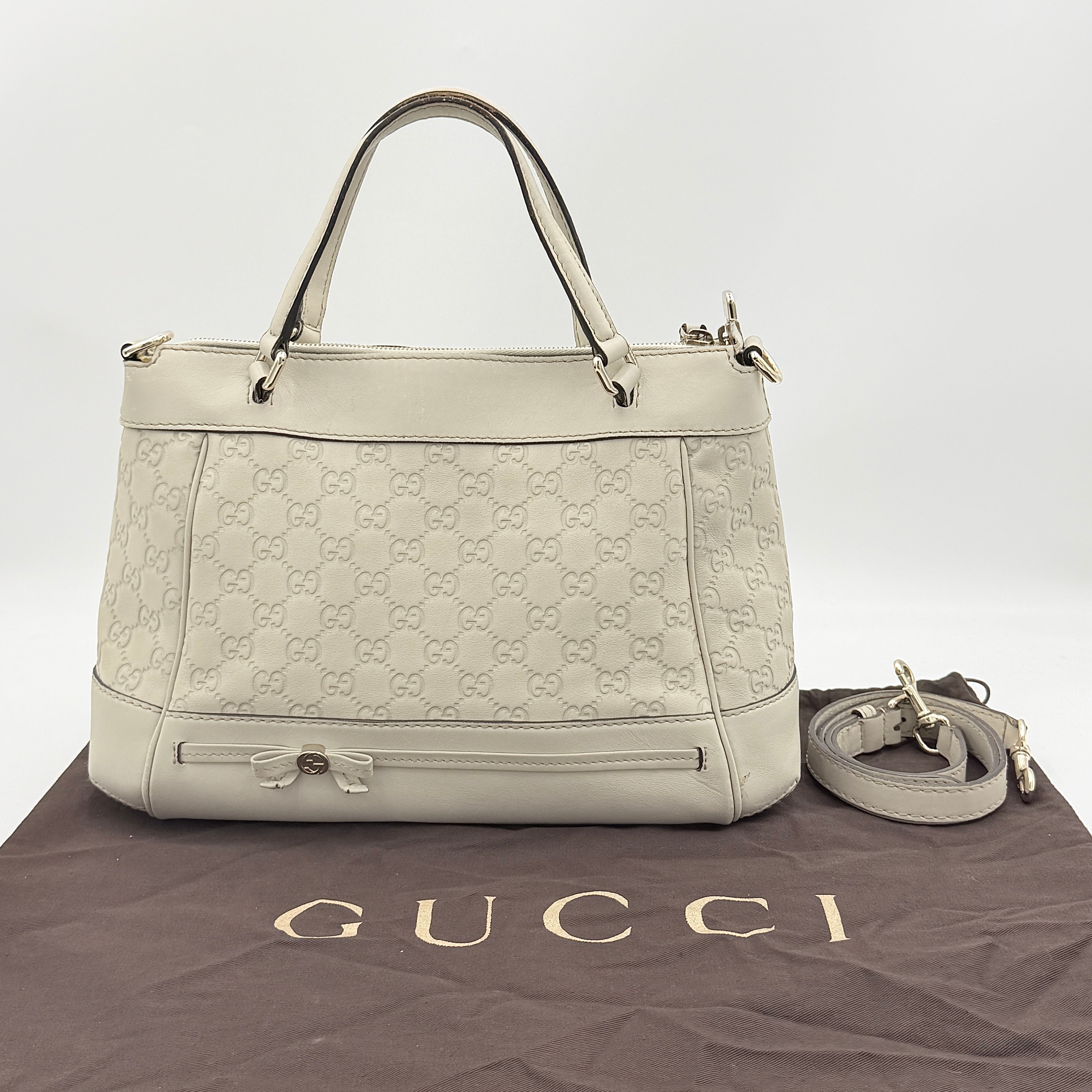 Gucci Mayfair Bow 2Way shoulder bag in cream GG monogram leather with dual handles and detachable strap, styled against a neutral backdrop.