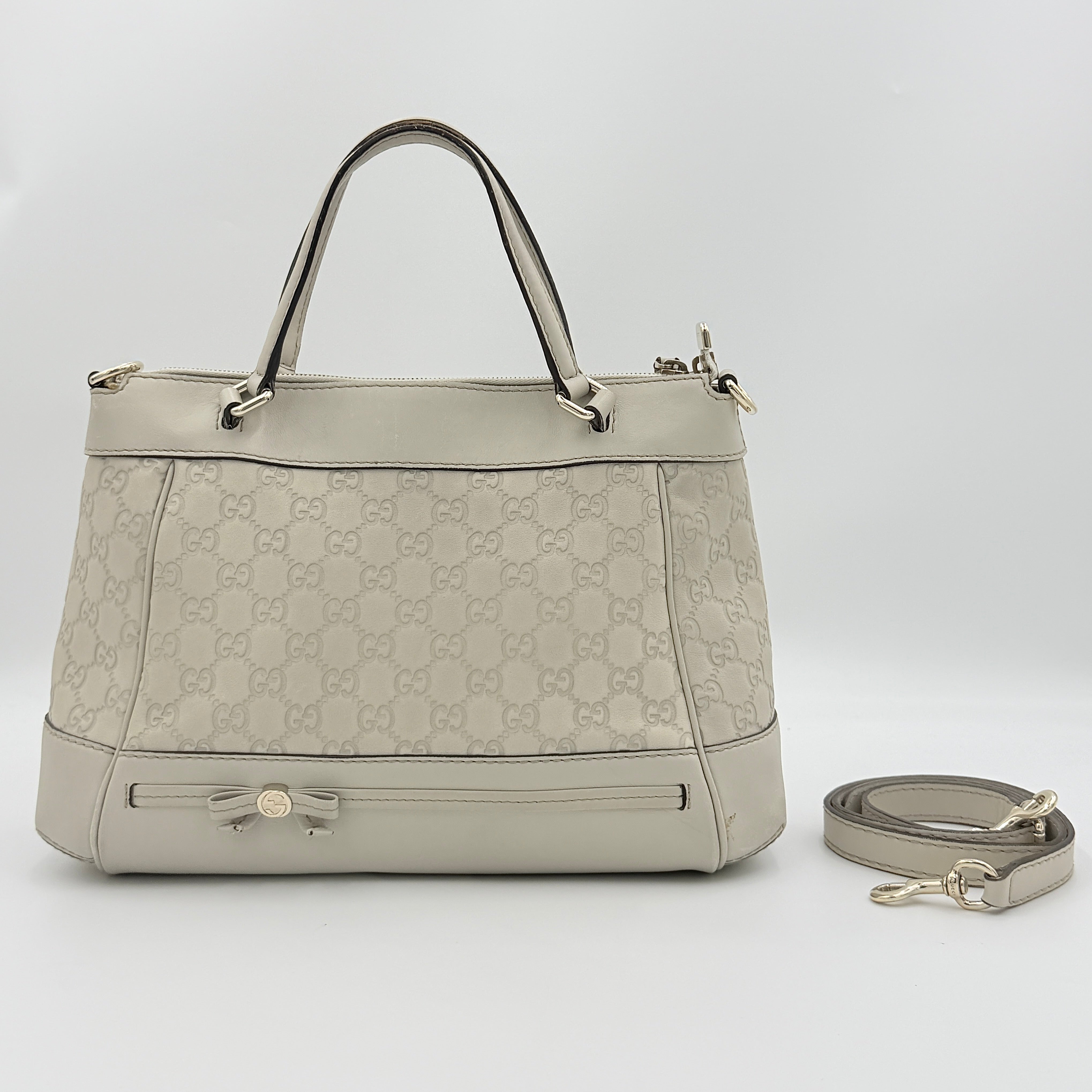 Gucci Mayfair Bow 2Way shoulder bag in cream GG monogram leather with dual handles and detachable strap, styled against a neutral backdrop.