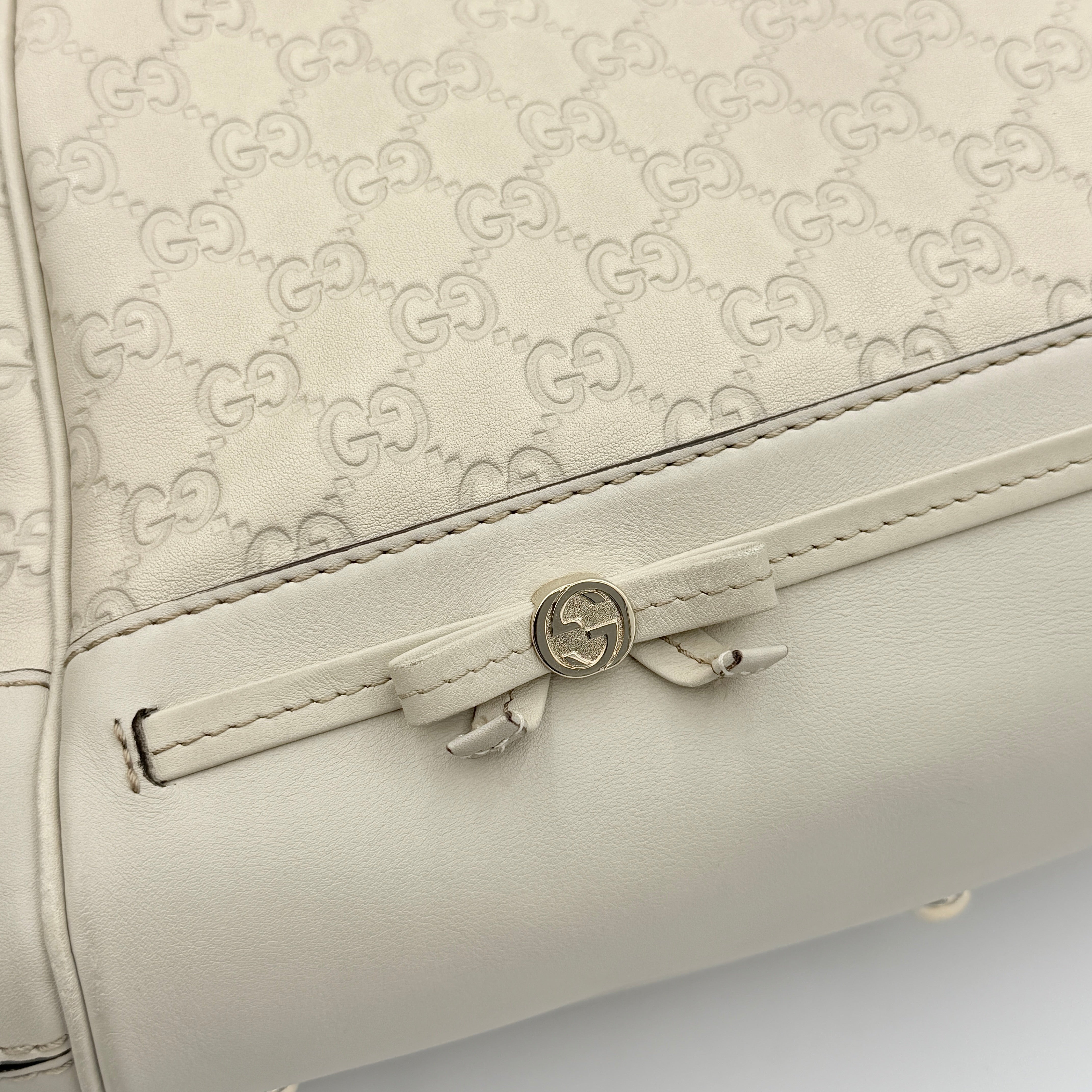 Gucci Mayfair Bow 2Way shoulder bag in cream GG monogram leather with dual handles and detachable strap, styled against a neutral backdrop.