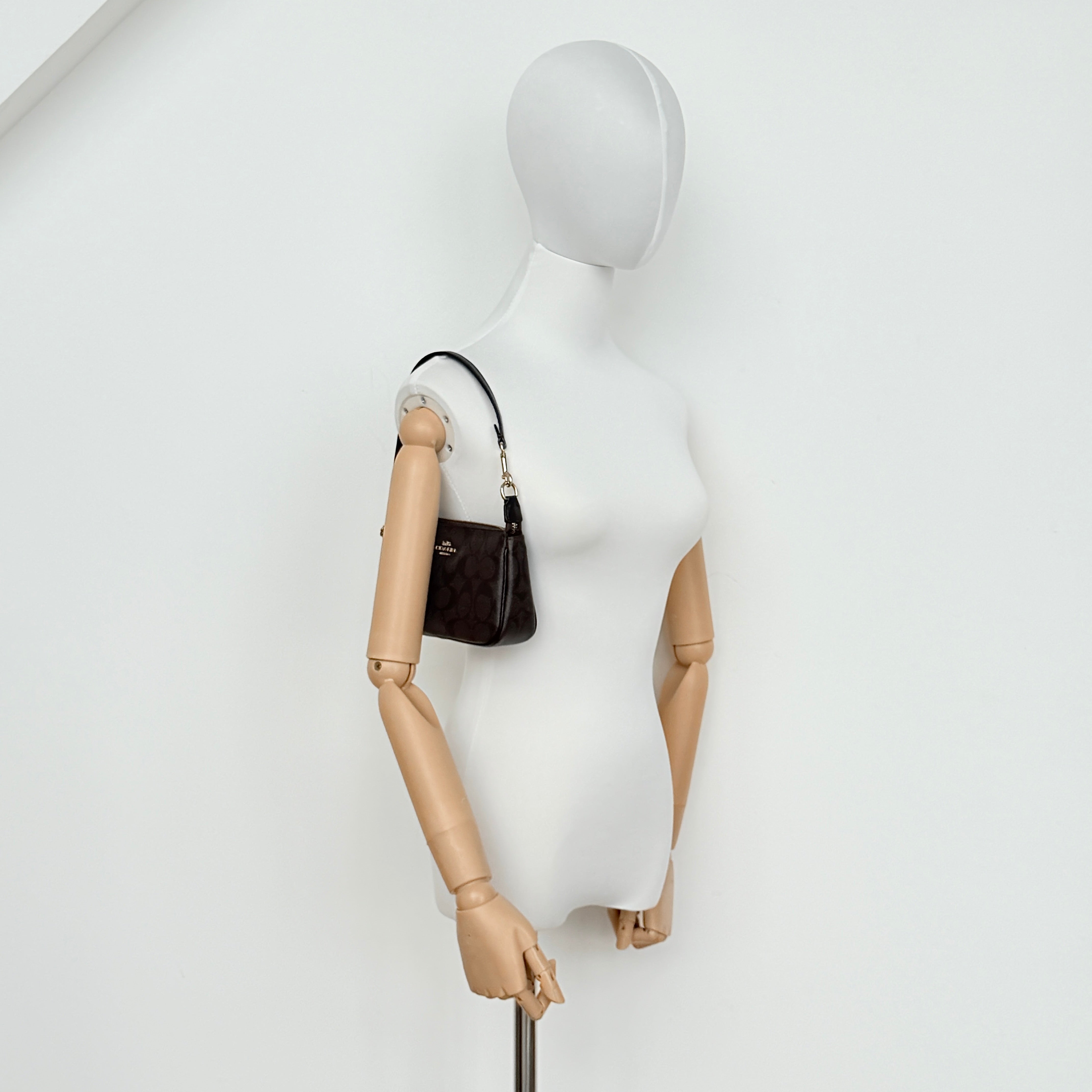 Coach Signature Nolita 19 shoulder bag in brown monogram canvas with black leather strap and gold-tone hardware, shown against a white background.