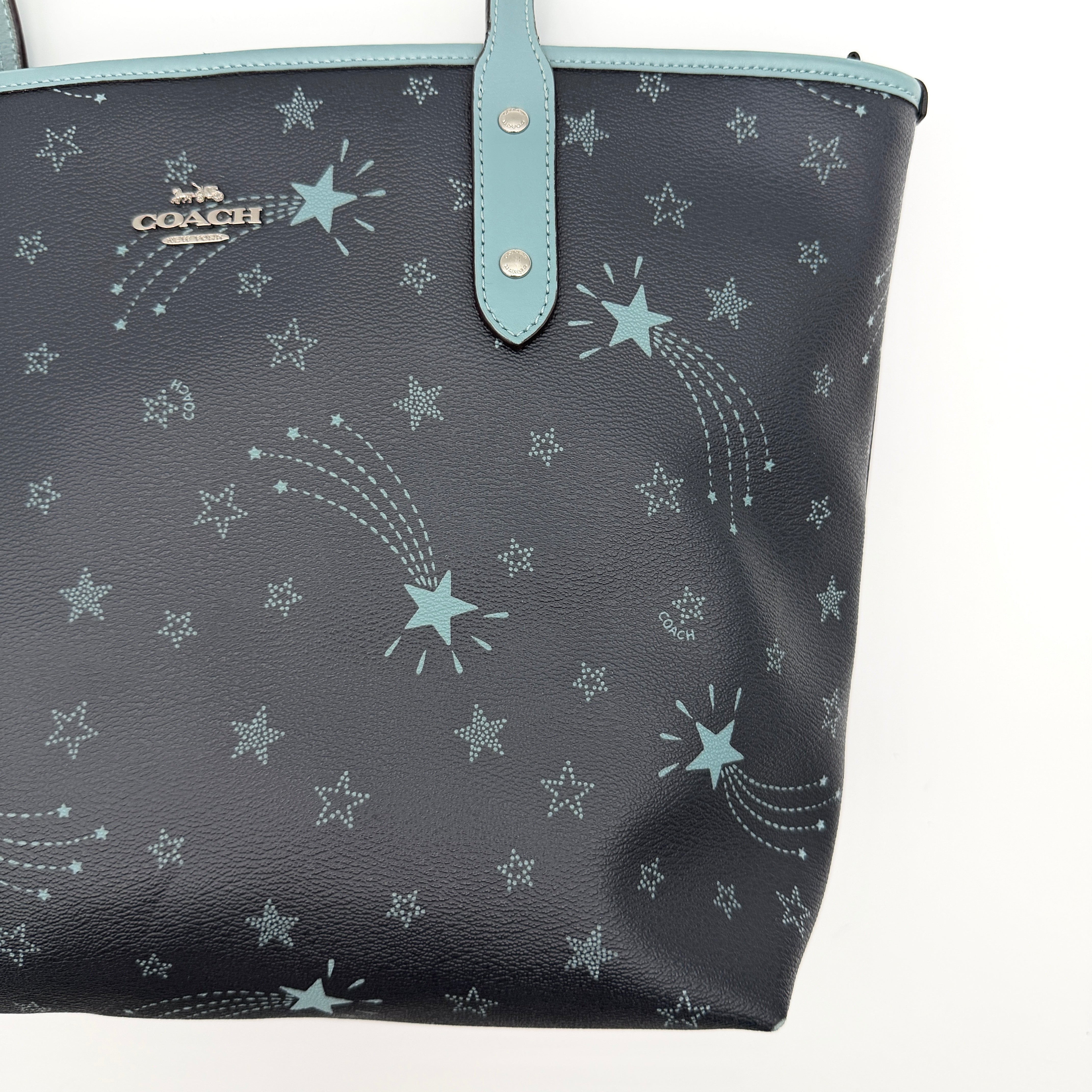 Coach Fiona Zip Tote in navy blue with star print and blue leather handles against a white background.