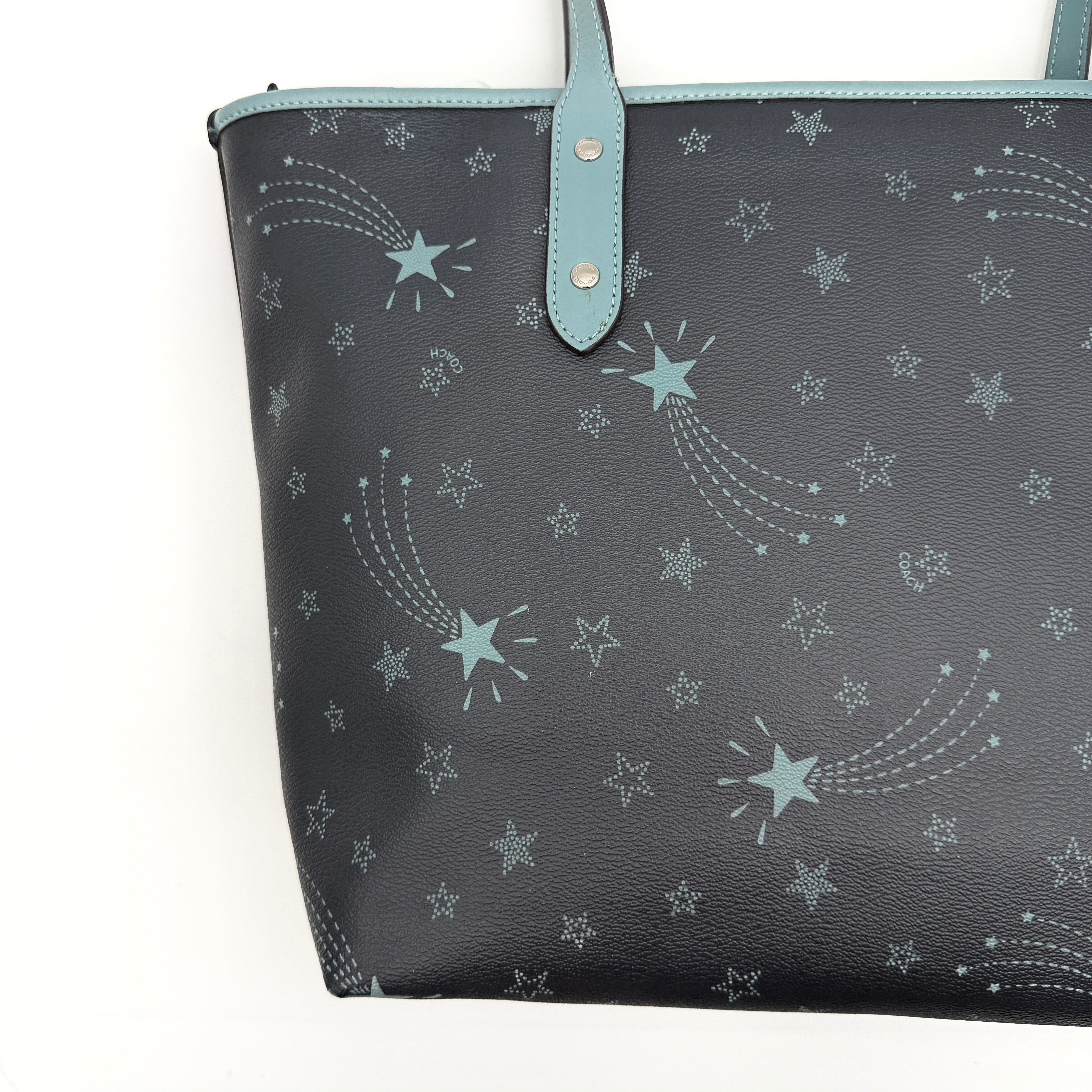 Coach Fiona Zip Tote in navy blue with star print and blue leather handles against a white background.