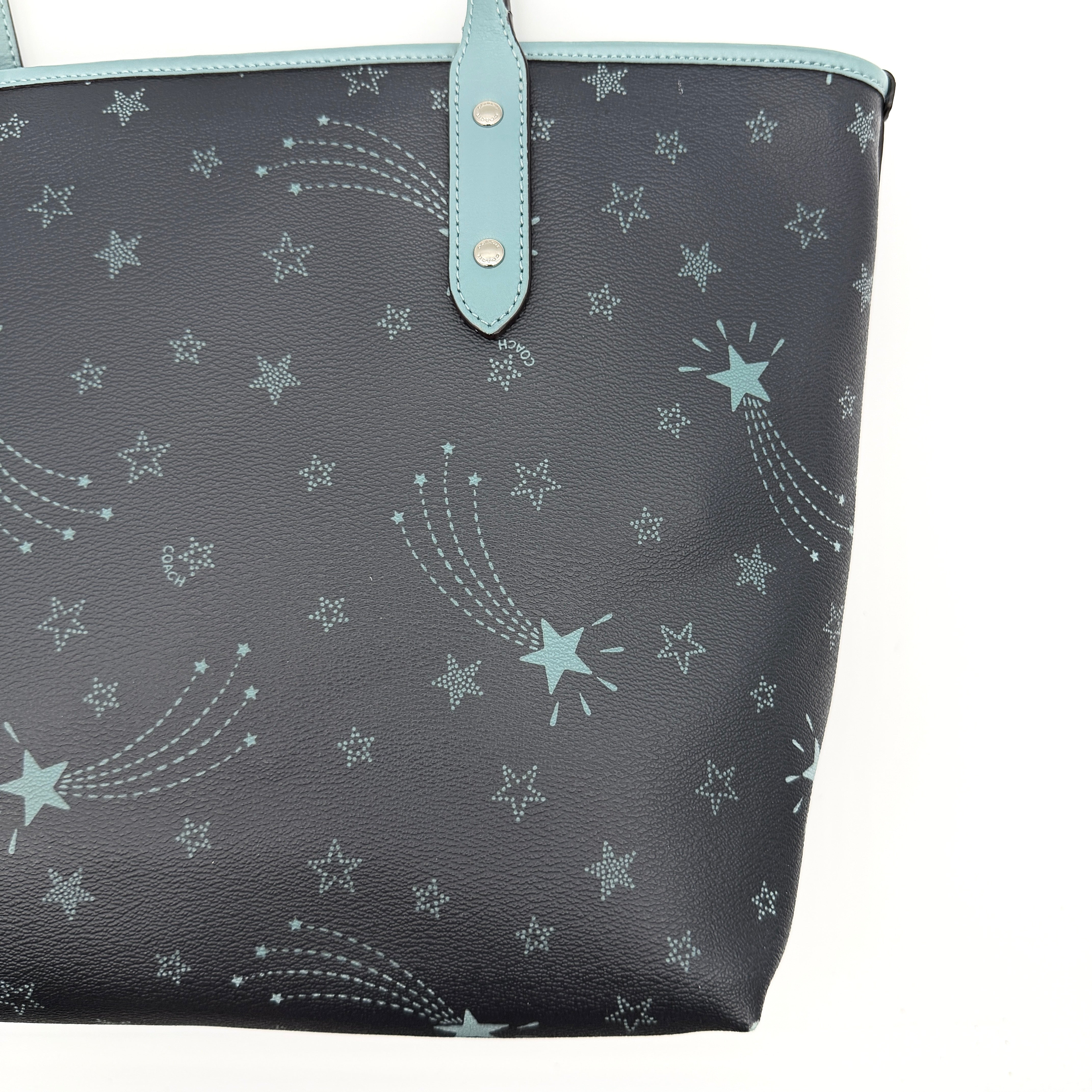 Coach Fiona Zip Tote in navy blue with star print and blue leather handles against a white background.