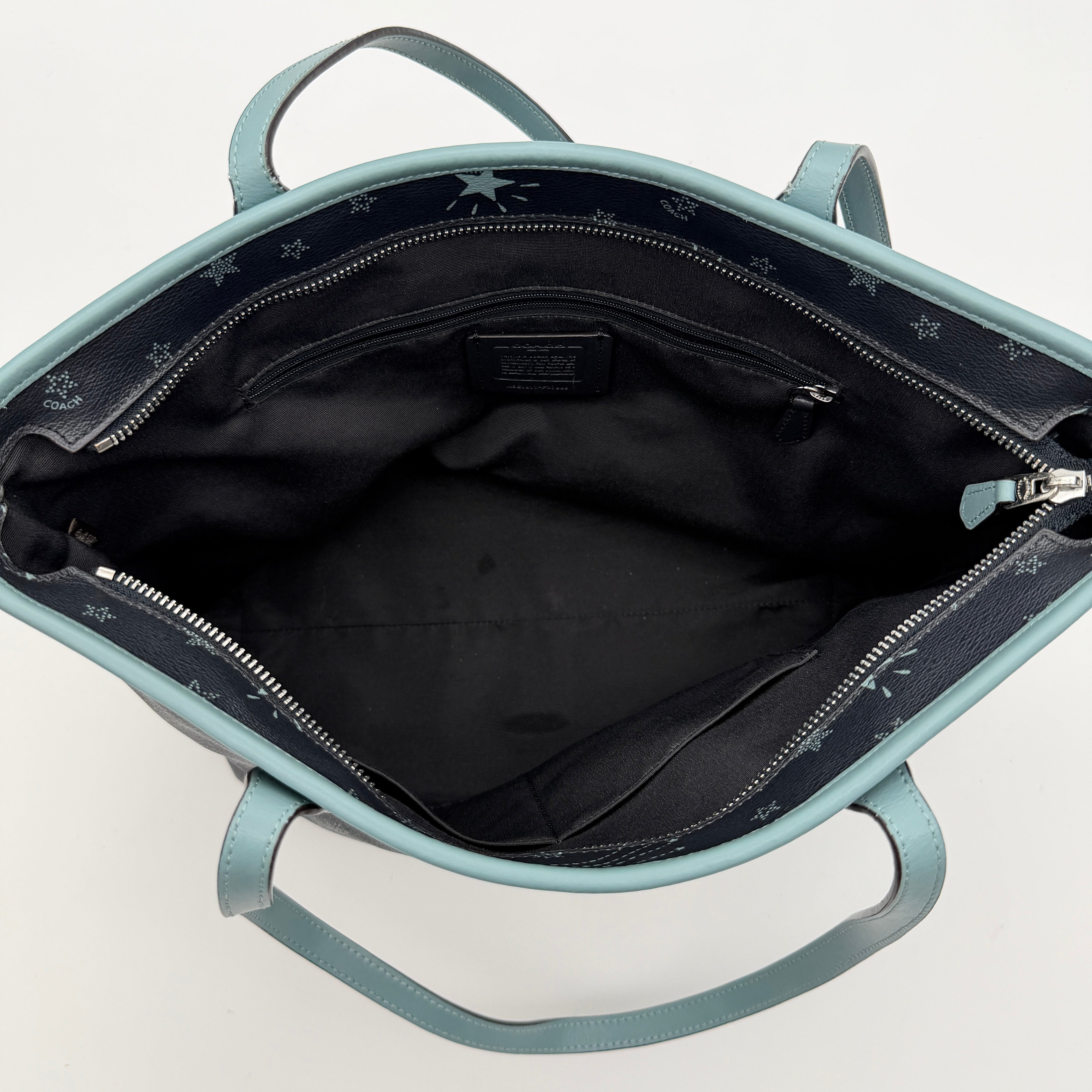 Coach Fiona Zip Tote in navy blue with star print and blue leather handles against a white background.