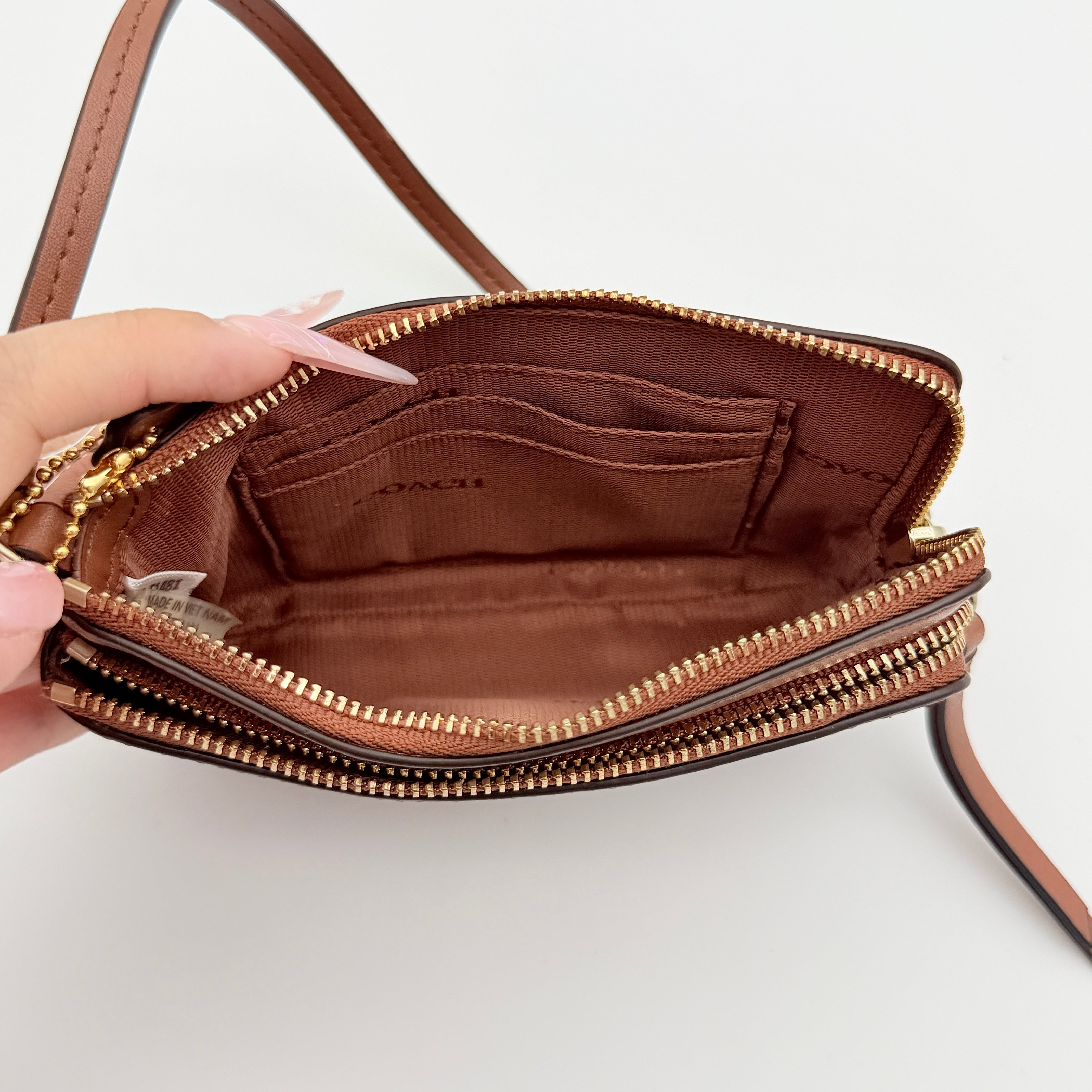 Coach Signature Double Zip Wristlet in brown leather with gold hardware and wrist strap, displayed with Coach cards.