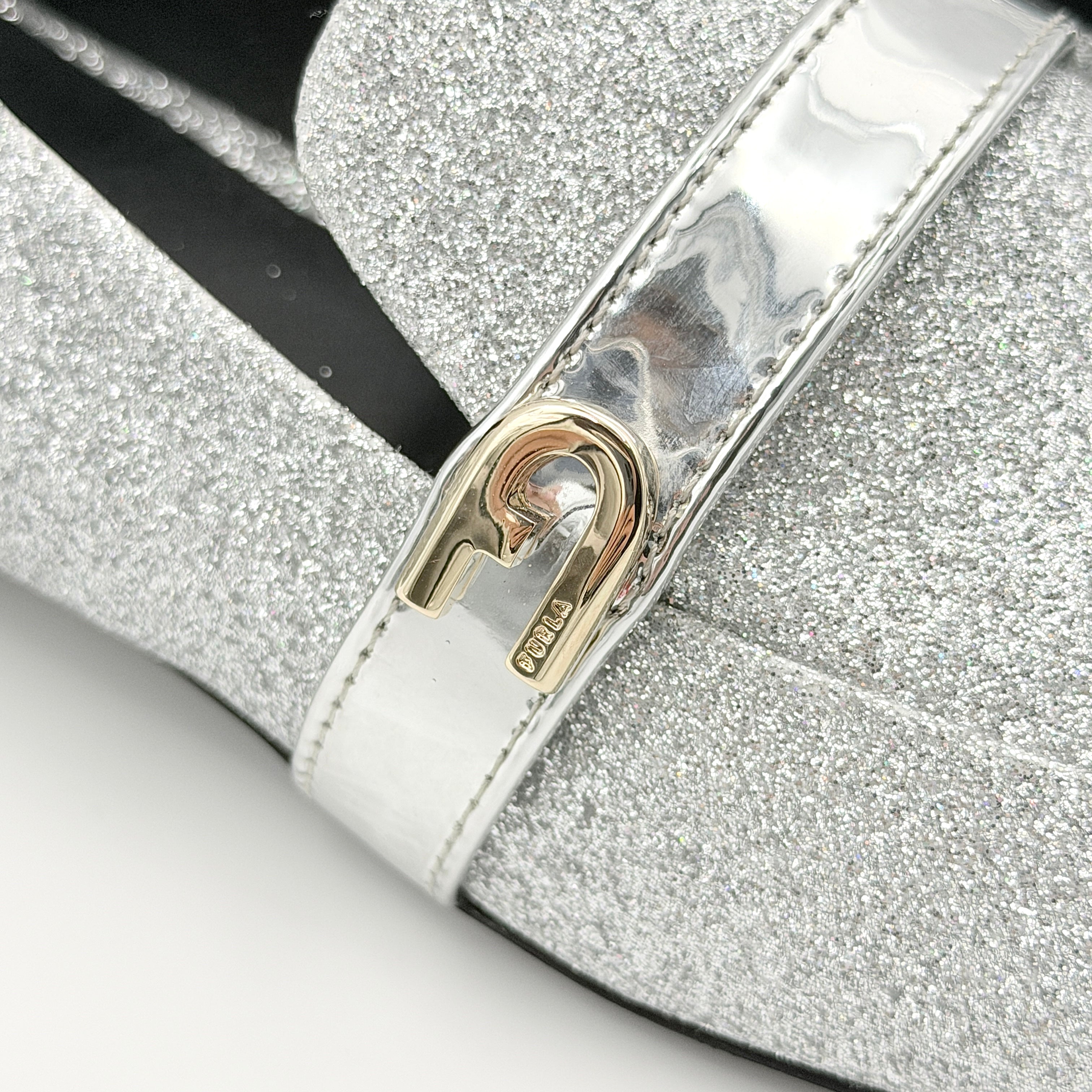 Furla 1927 T.20 loafers in silver microglitter with metallic strap and gold-tone detail, displayed in a three-quarter view.