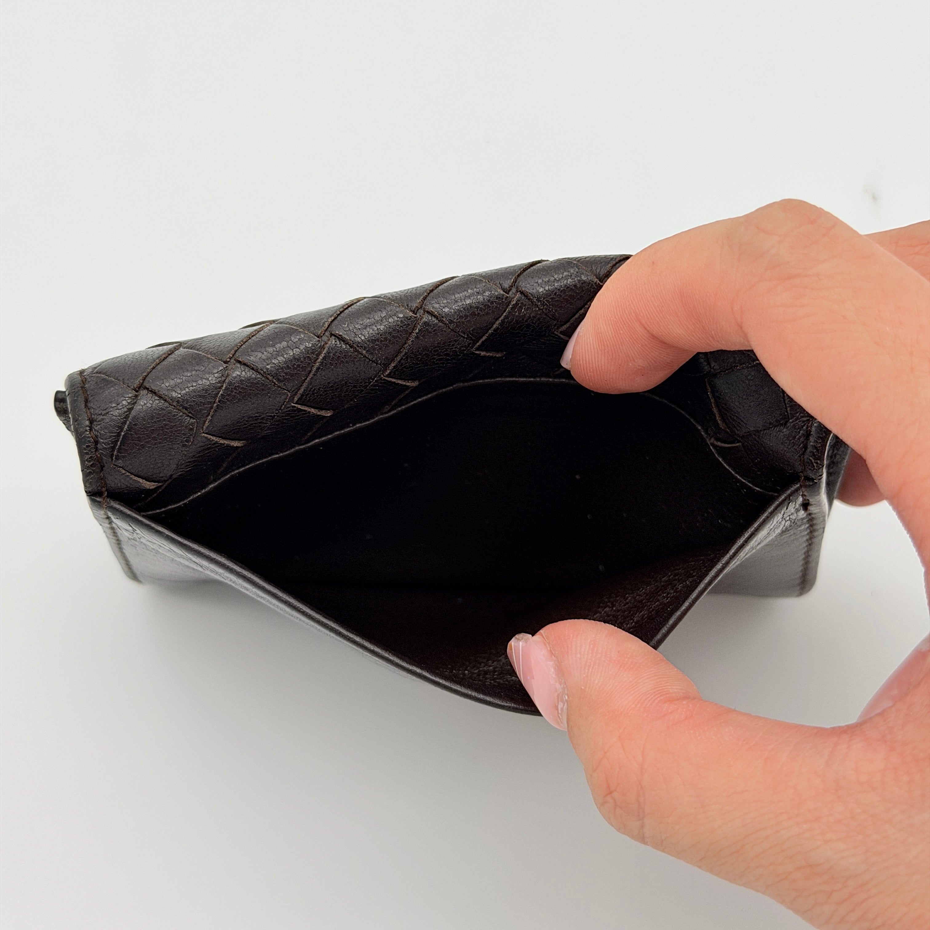 Bottega Veneta Intrecciato card case in black leather with woven front, photographed against a white background.