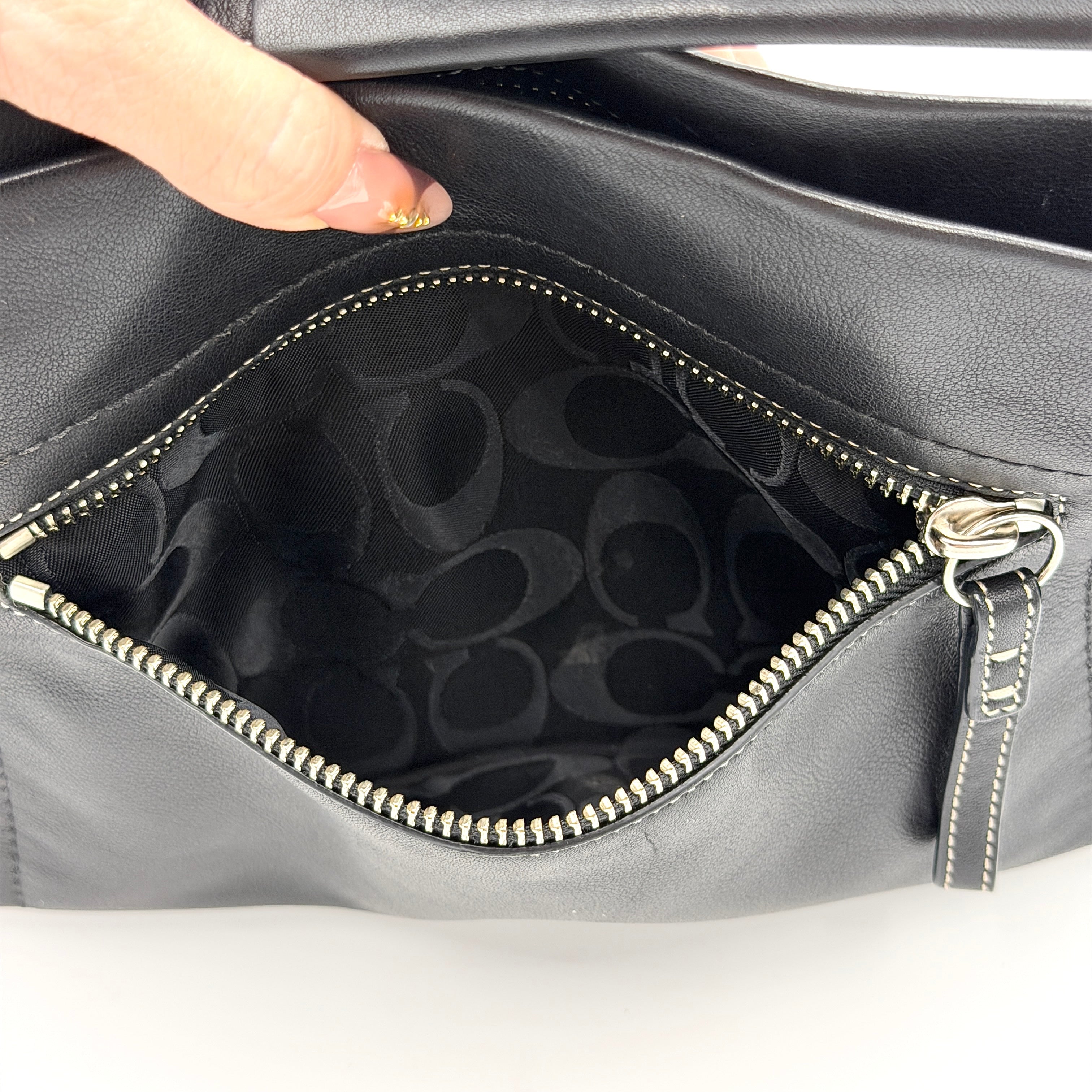 Coach Signature East West Shoulder Bag in black leather with silver hardware and contrast stitching, displayed on a white background.