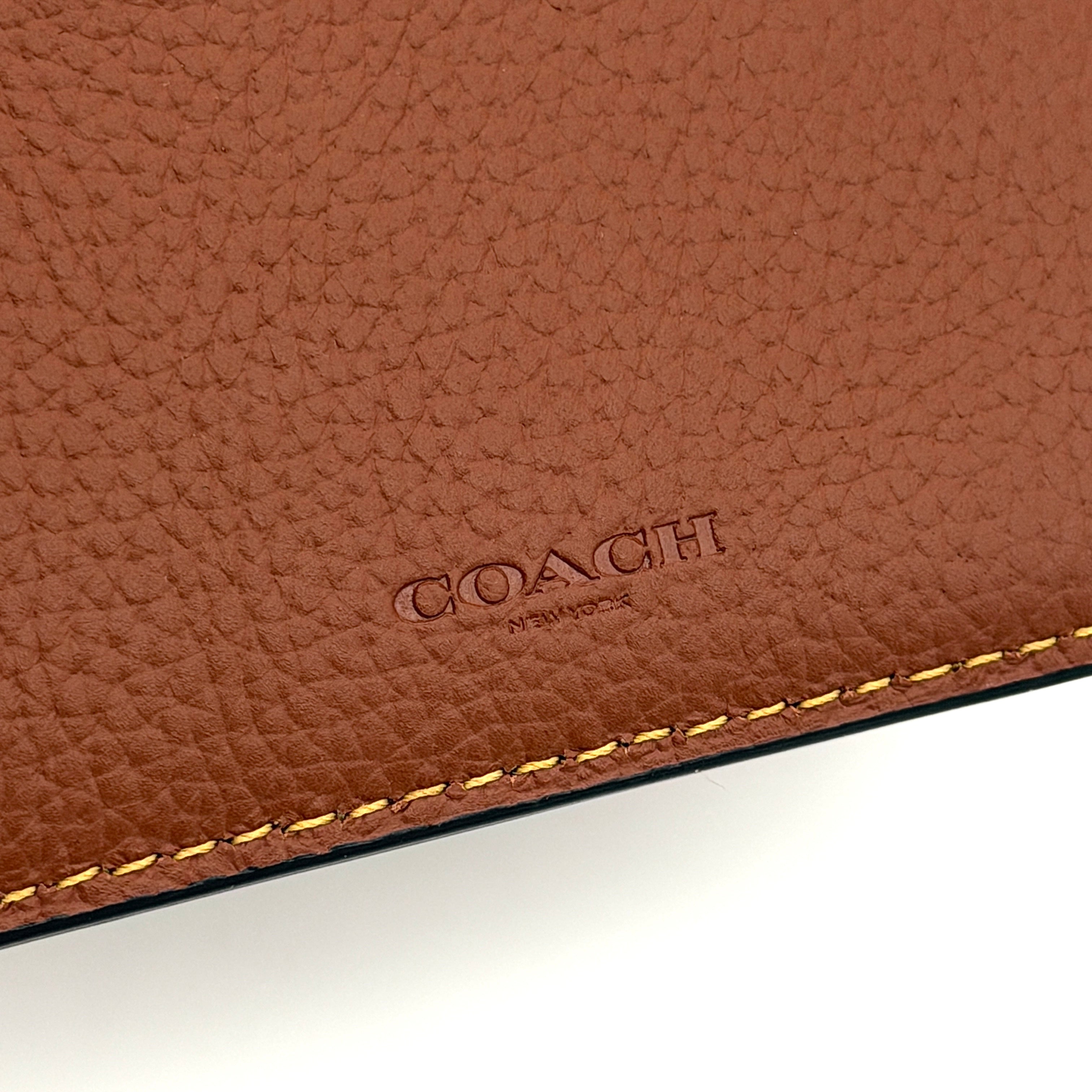 Coach slim billfold wallet in saddle brown pebbled leather with embossed logo and refined topstitch detailing.