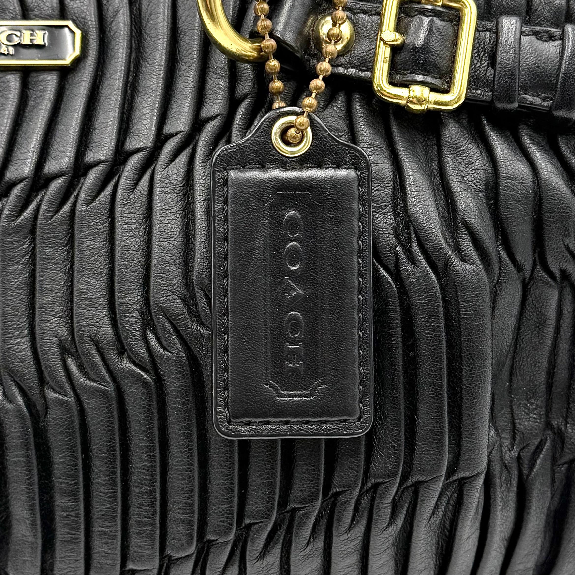 Coach Signature Madison shoulder bag in pleated black leather with gold hardware and dual handles.