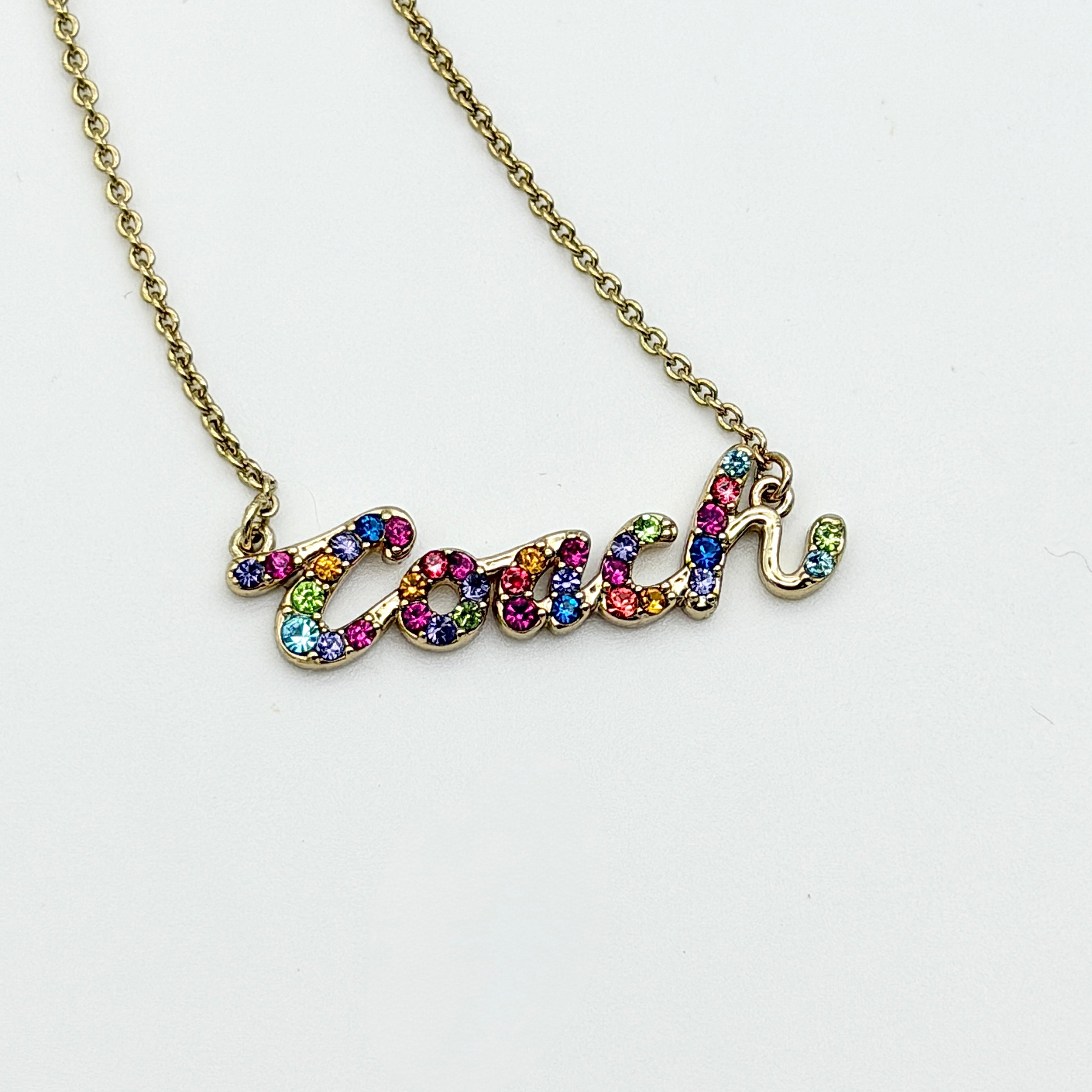 Coach Signature Script Rainbow Necklace with multicolour crystals set on a gold-tone chain, displayed in its original Coach box.