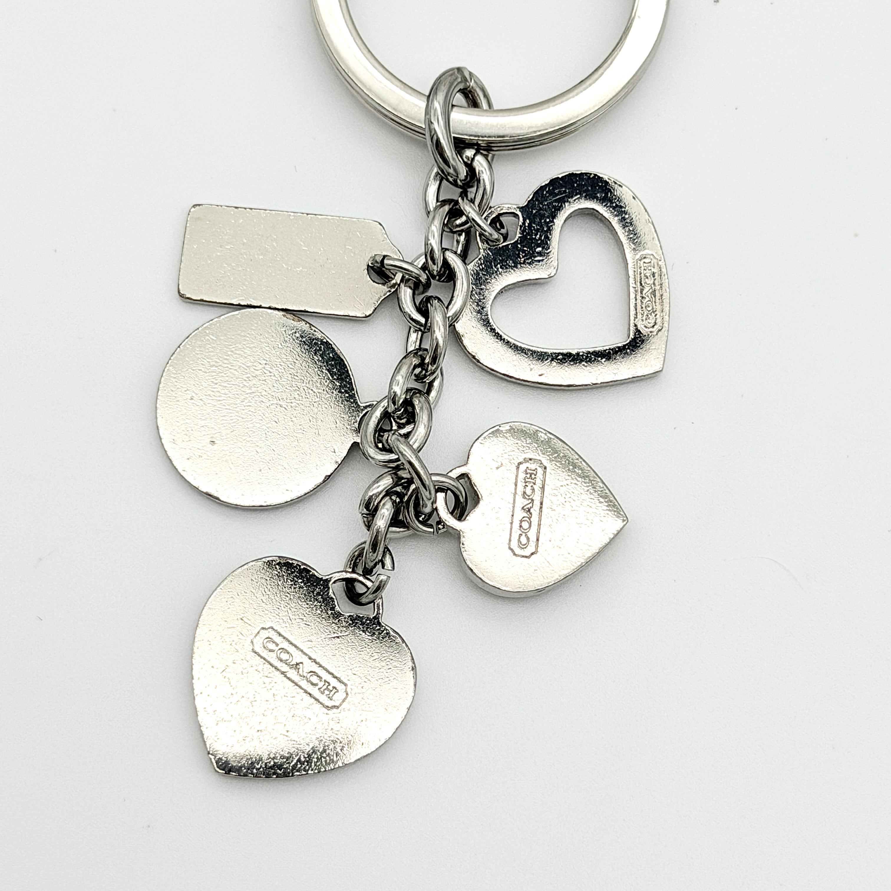 Coach Triple Heart Crystal Charms Keychain in purple and silver-tone, displayed on a Coach-branded drawstring pouch.