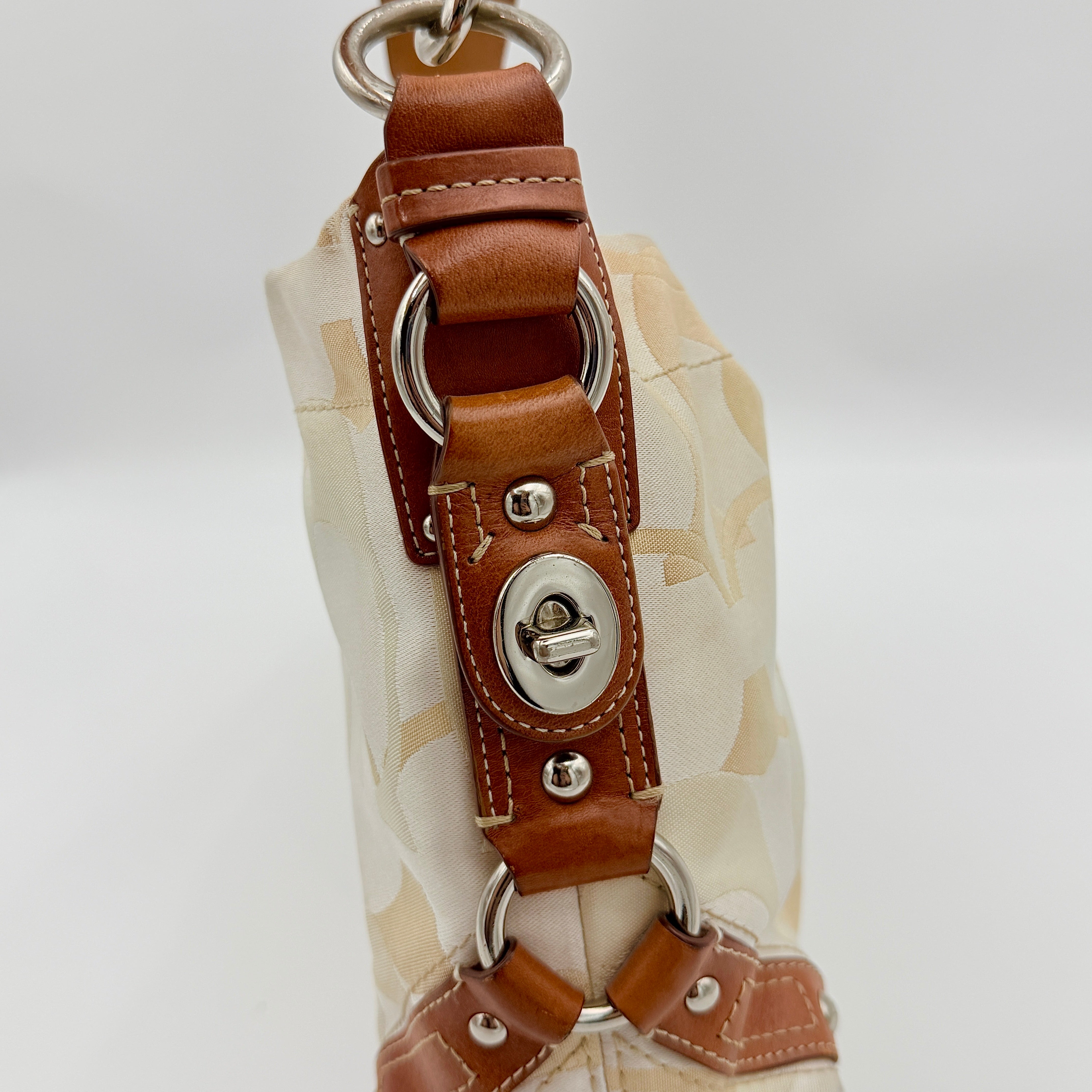Coach Signature Carly Hobo shoulder bag in cream and brown canvas with tan leather trim and chain-detailed strap.