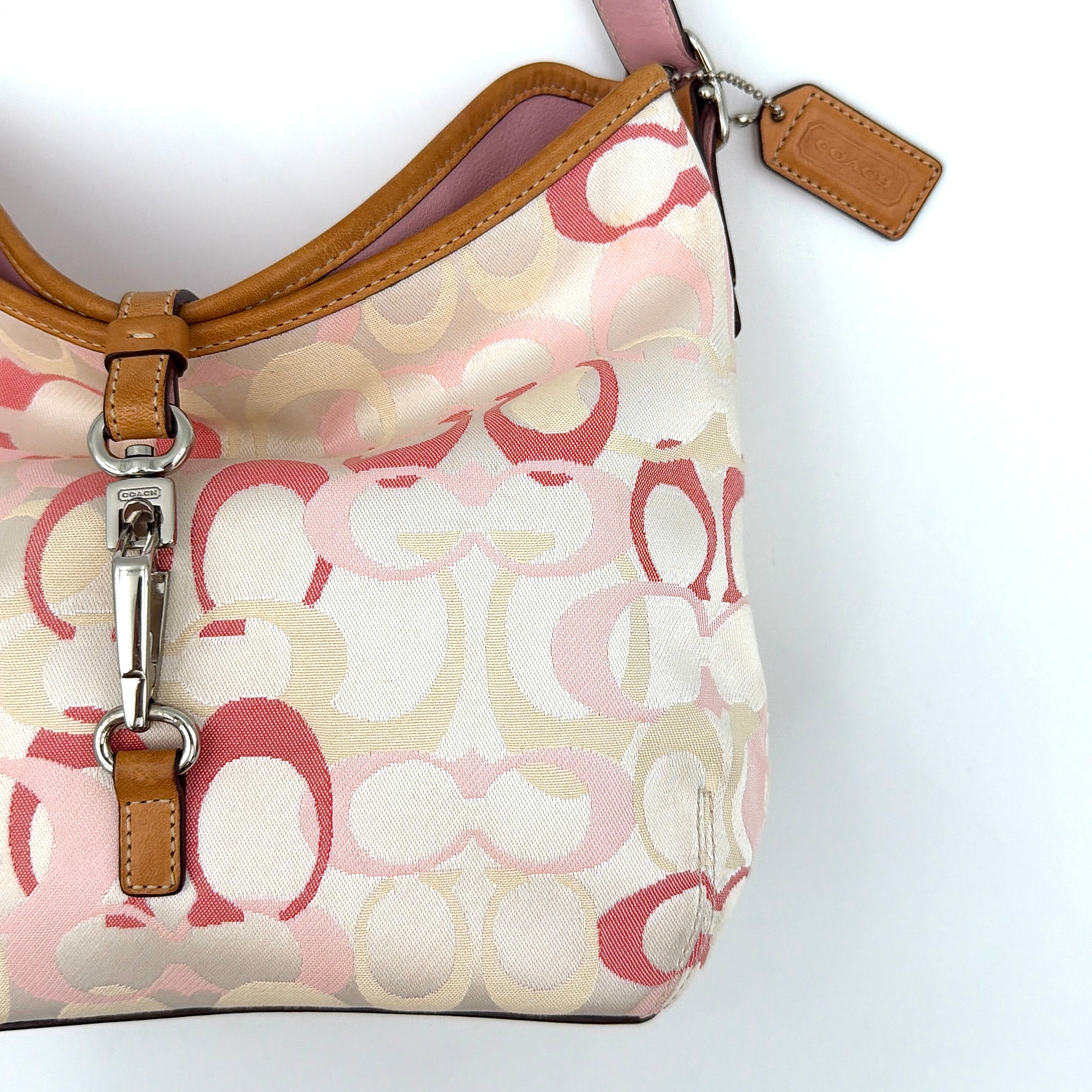 Coach hobo handbag in pink-cream canvas with signature C motif and tan leather trim, featuring a silver clip detail and a structured silhouette.