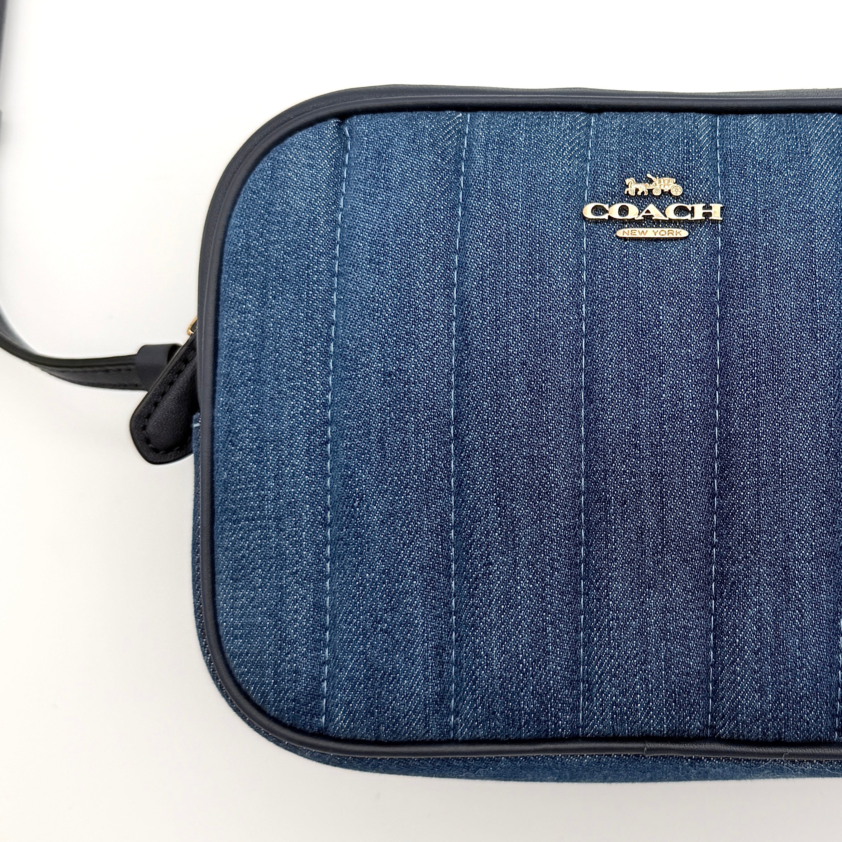 Coach Jamie Mini Camera Bag in quilted blue denim with navy leather trim and gold hardware, shown with its adjustable crossbody strap.