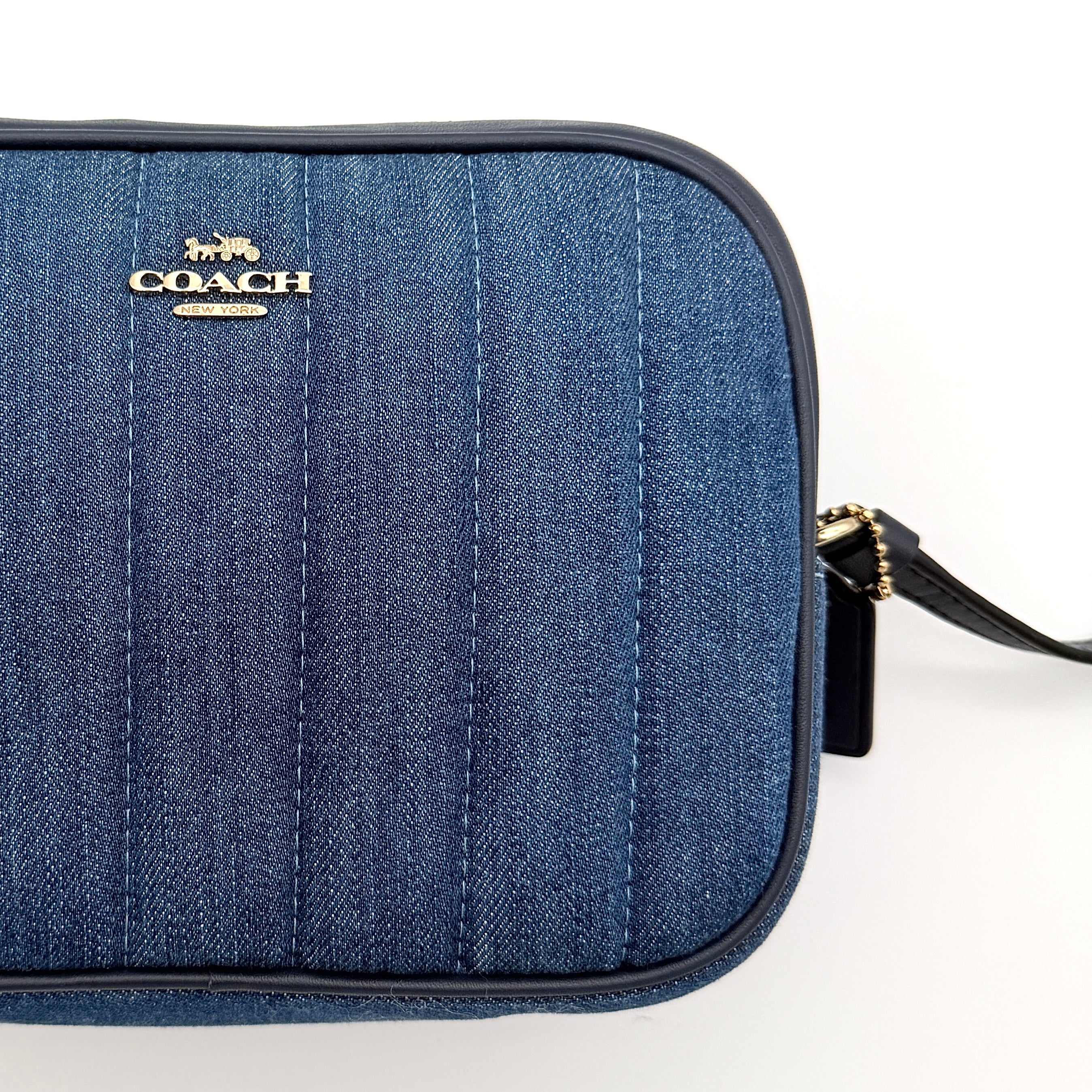 Coach Jamie Mini Camera Bag in quilted blue denim with navy leather trim and gold hardware, shown with its adjustable crossbody strap.