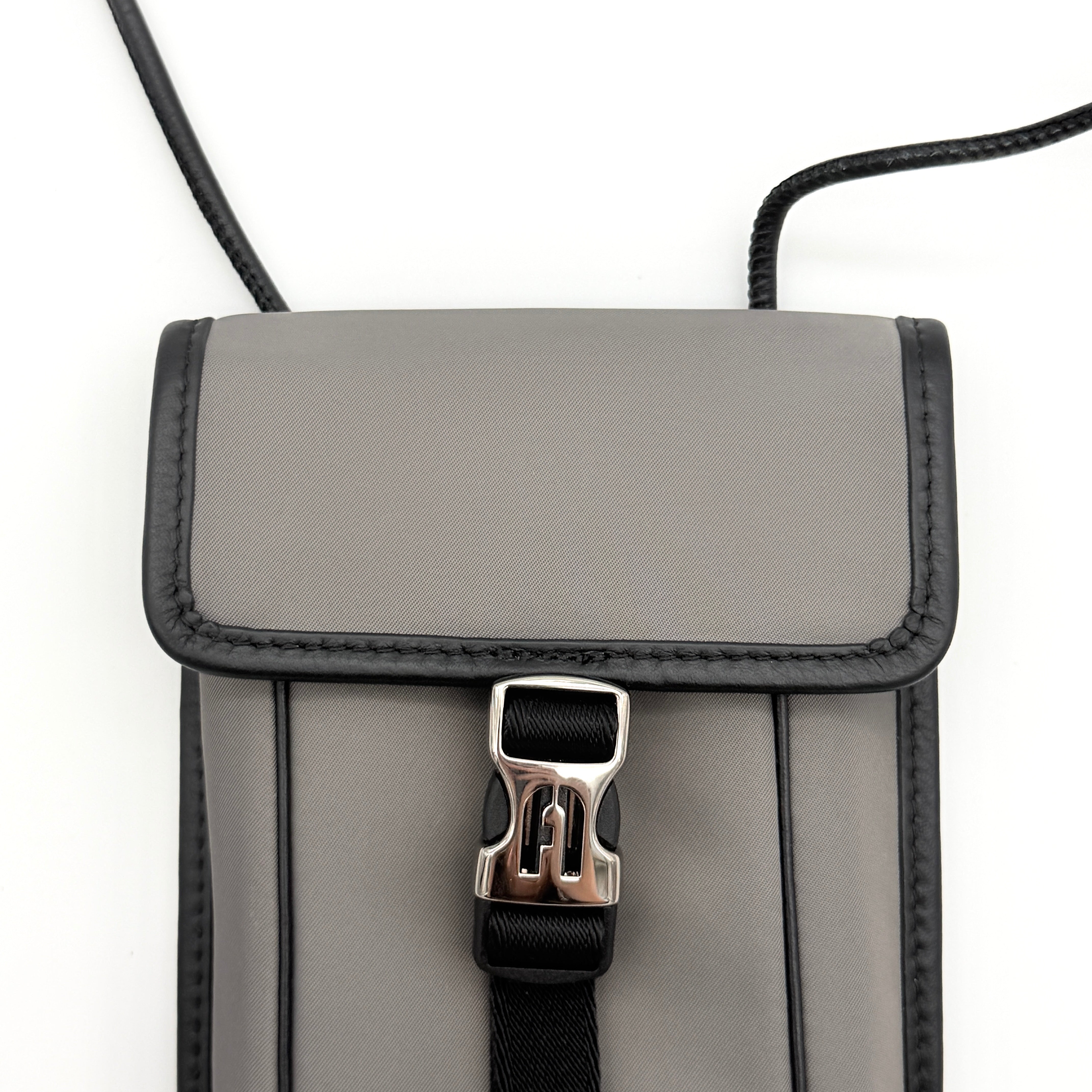 Furla Cosmo grey phone holder with black trim, silver buckle, and black cord strap on white background.