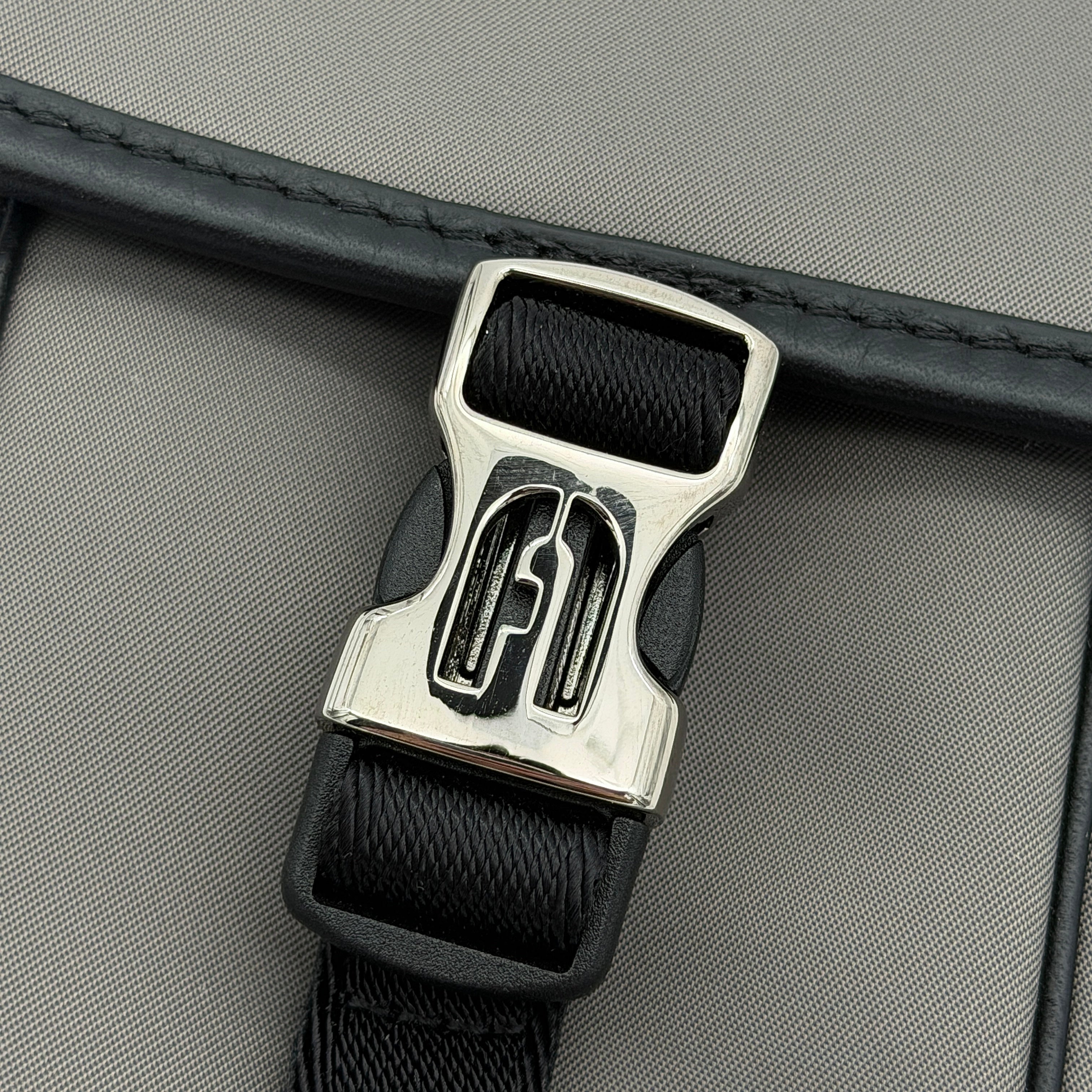 Furla Cosmo grey phone holder with black trim, silver buckle, and black cord strap on white background.