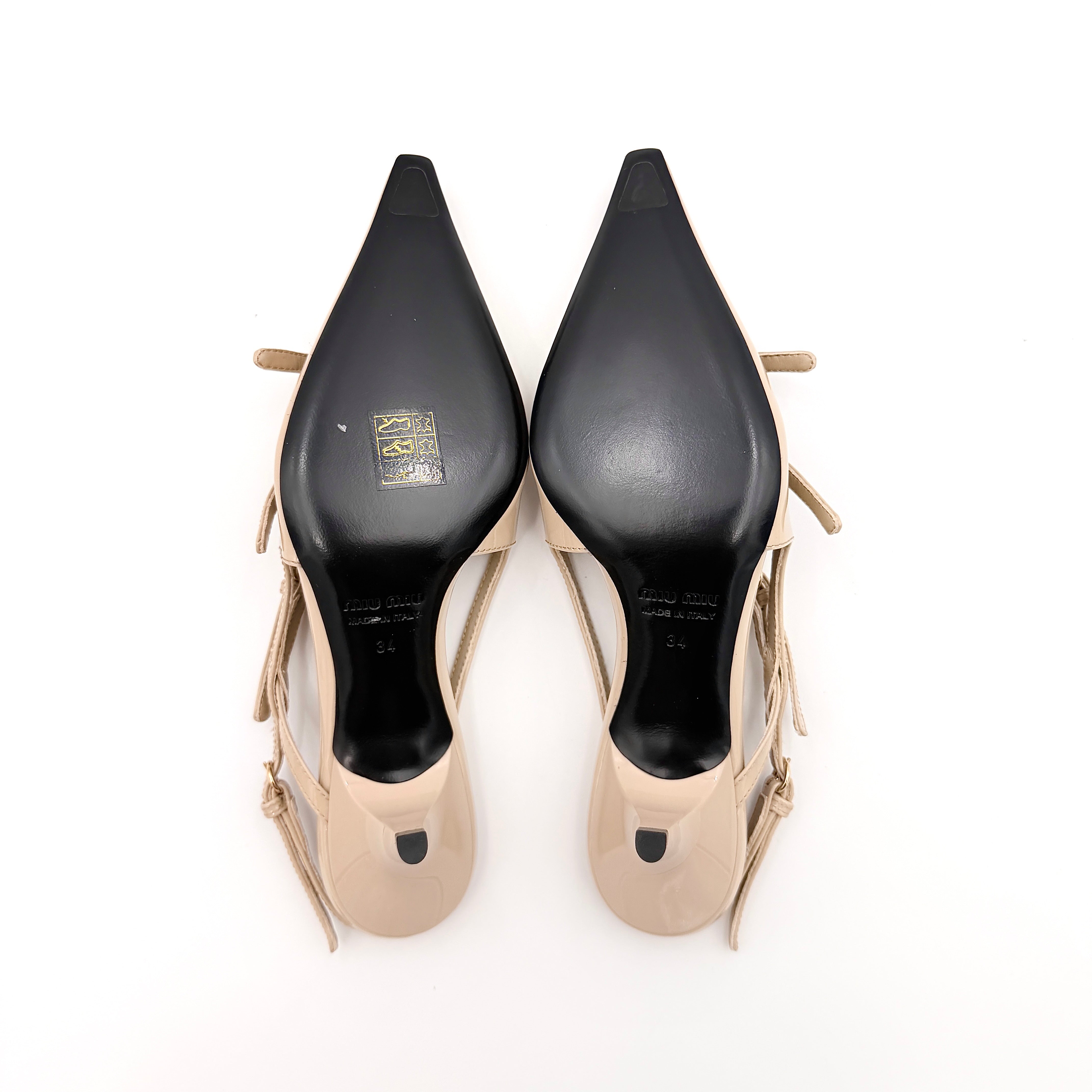 A pair of Miu Miu beige patent leather slingback pumps with pointed toes and gold-tone buckles displayed on a white background.