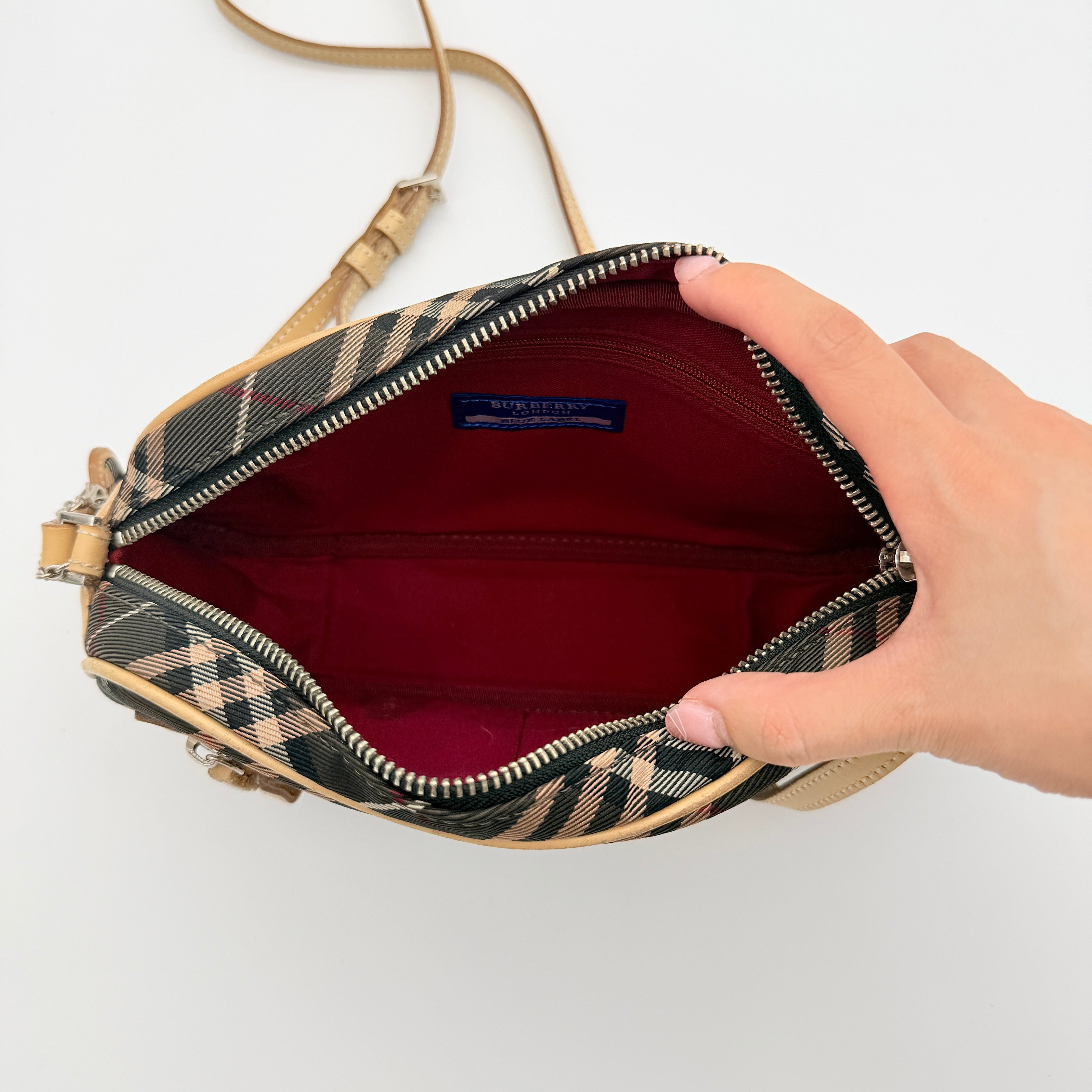 Burberry Blue Label Nova Check crossbody bag with tan leather trim and heart charm, styled on a white background.