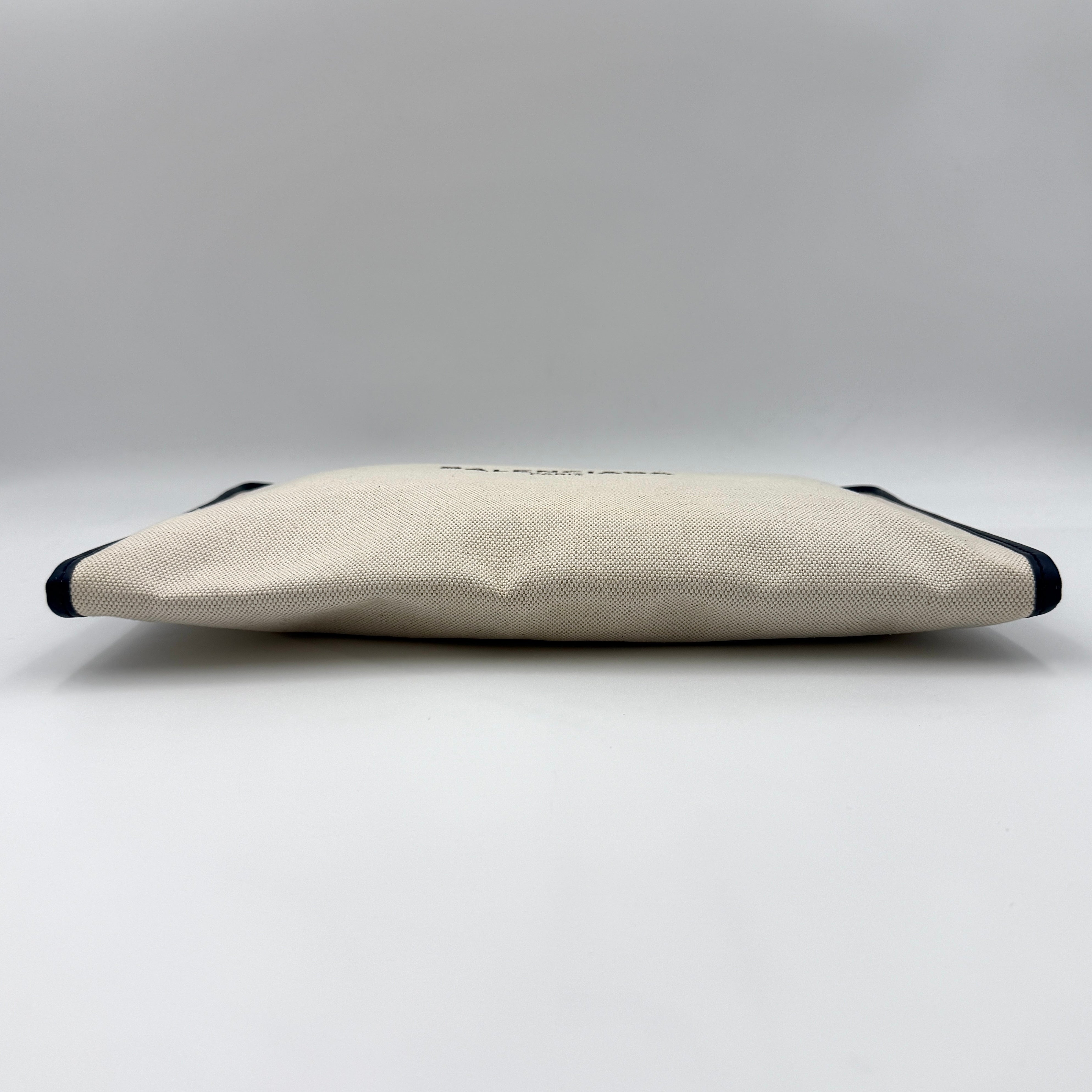 Balenciaga large ivory canvas clutch with black leather trim and logo, shown against a plain background.