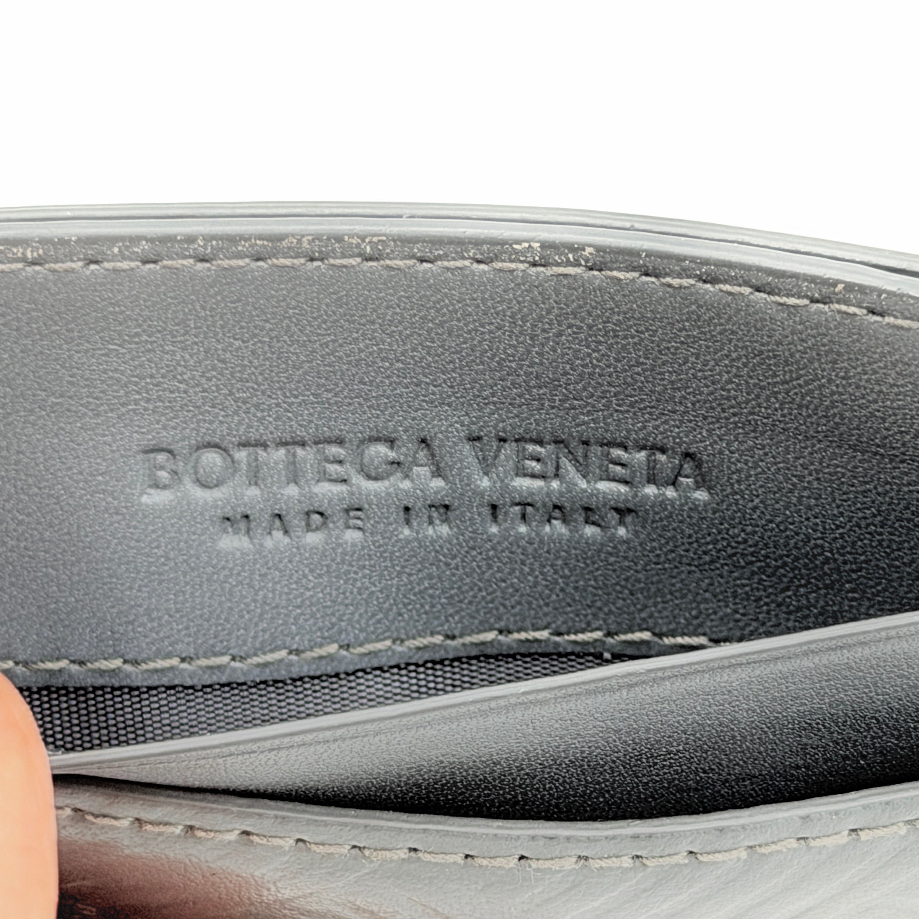 Bottega Veneta grey leather card holder with embossed geometric weave detail, photographed against a white background.