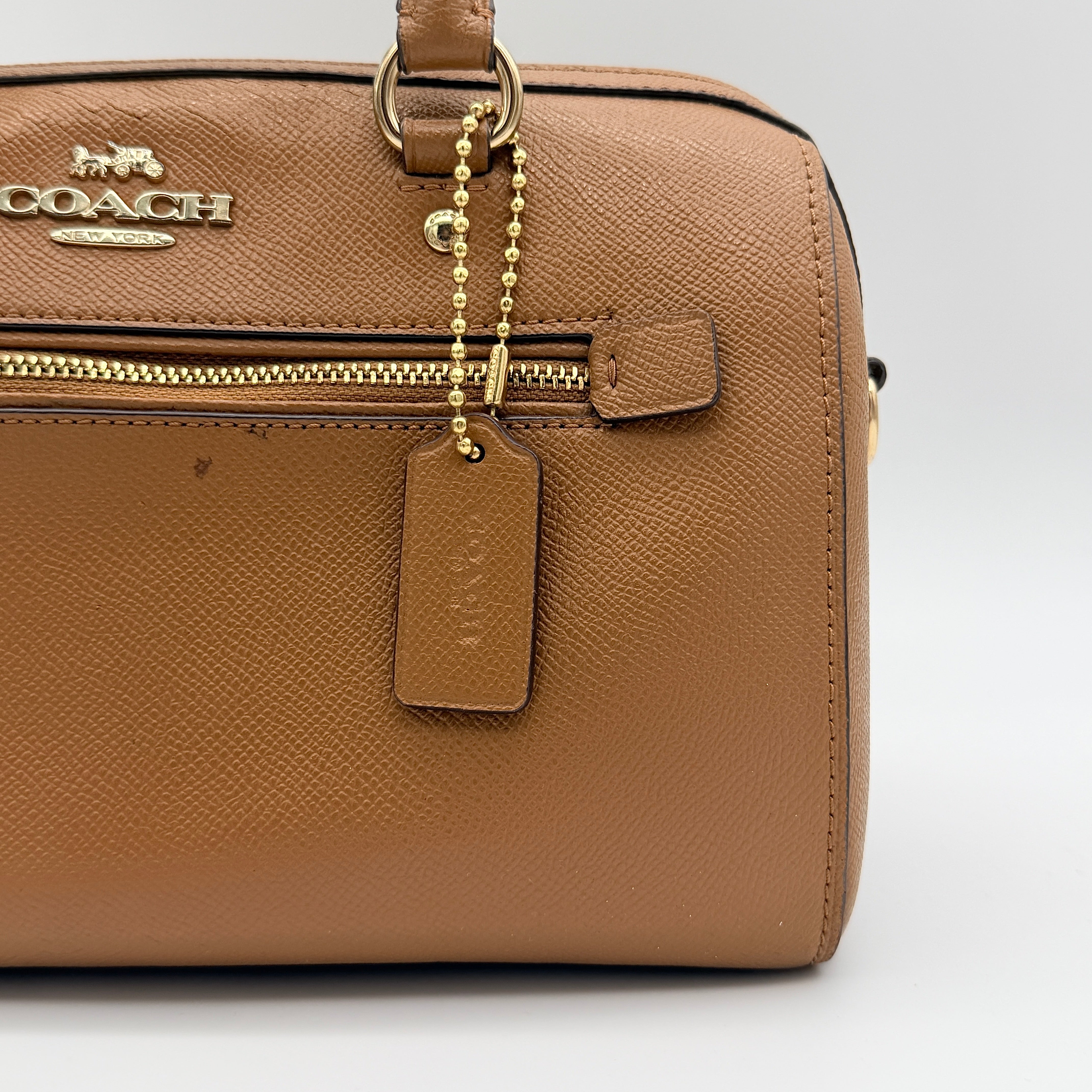 Coach Rowan satchel in brown grained leather with gold hardware, shown with dust bag, strap, and care cards.