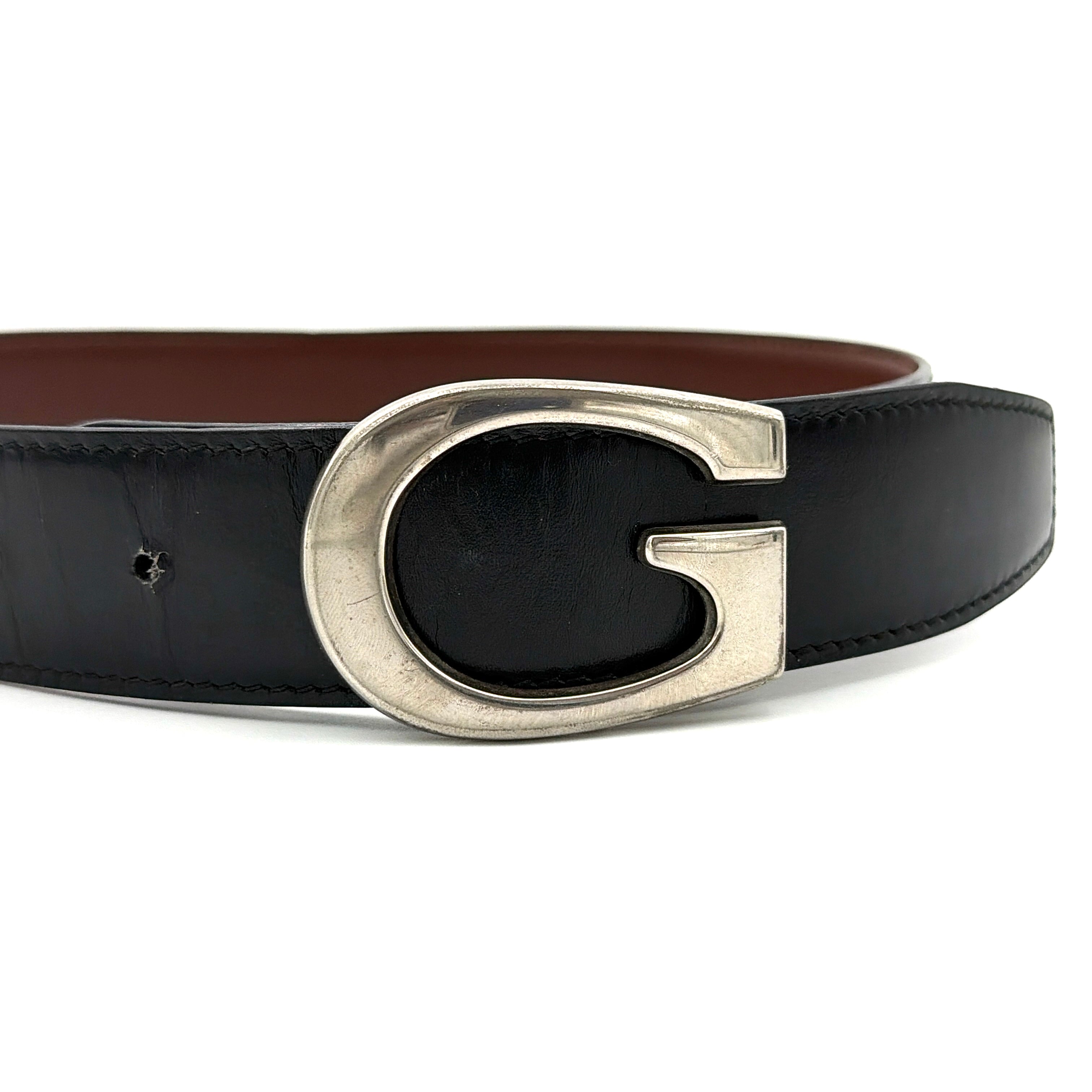 Gucci black leather belt with an oversized silver metal G logo buckle displayed in a curved profile.