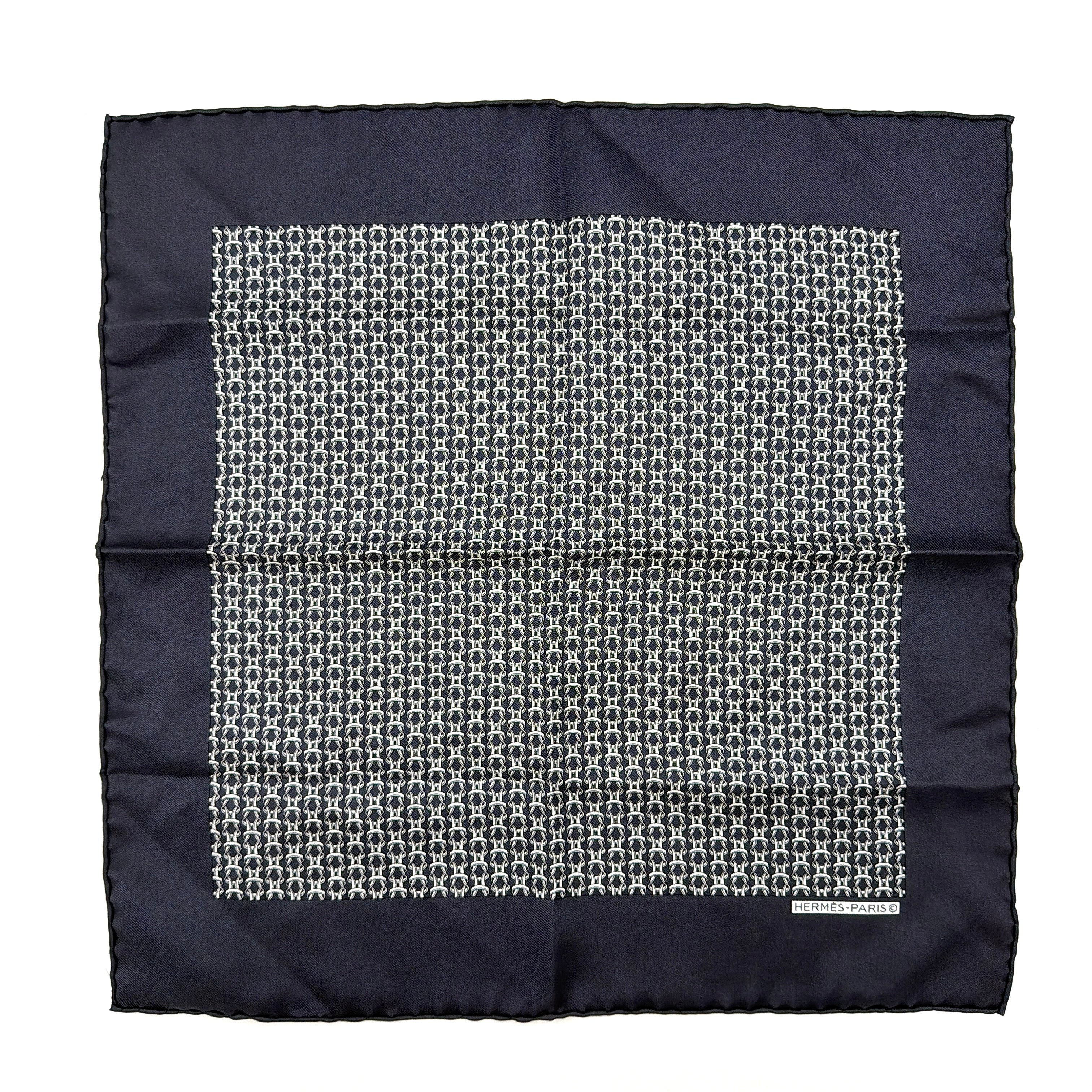Hermès silk scarf in navy blue with a white chain link pattern and bold border, elegantly displayed flat.