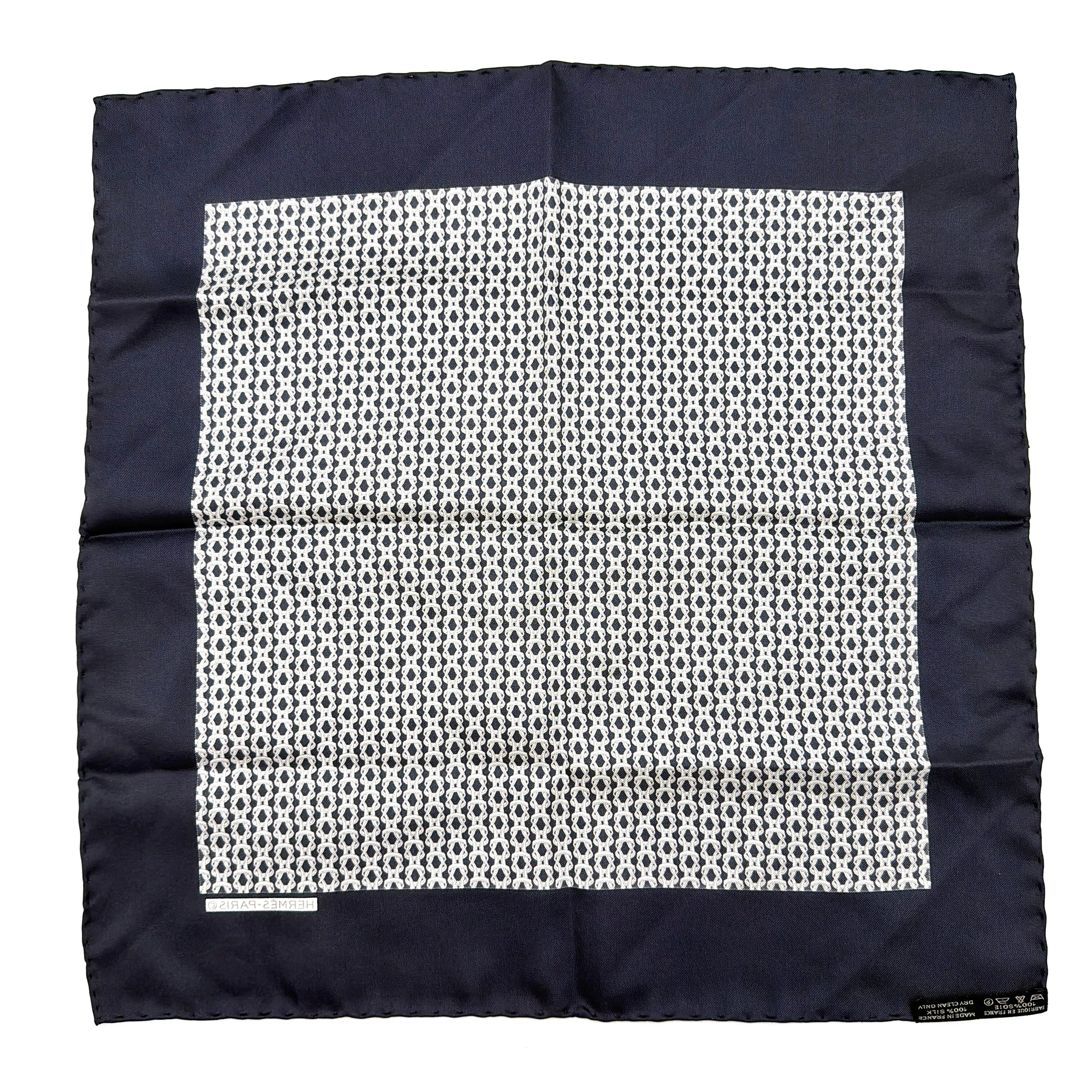 Hermès silk scarf in navy blue with a white chain link pattern and bold border, elegantly displayed flat.