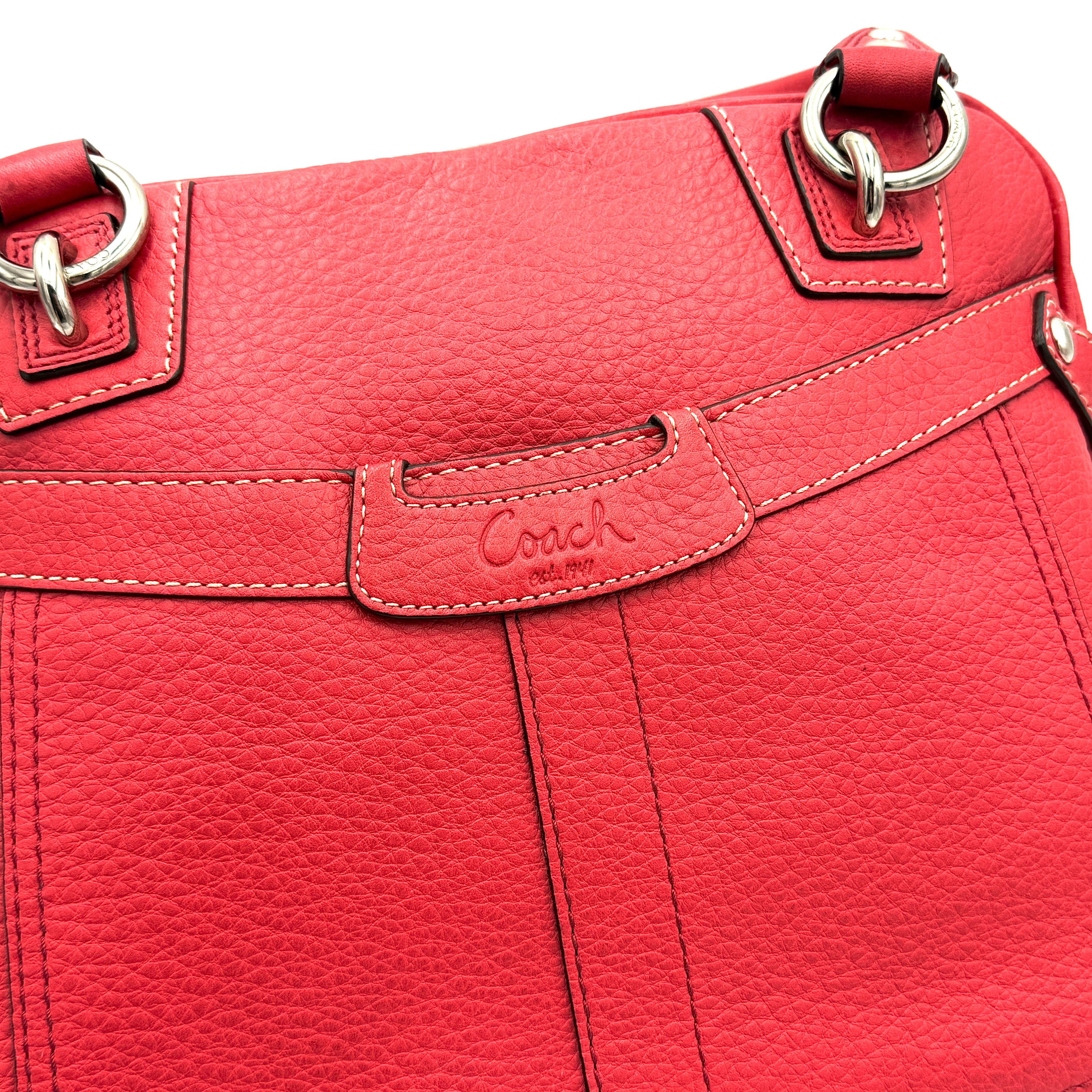 Coach red pebbled leather satchel with dual rolled handles, silver hardware, and structured silhouette.