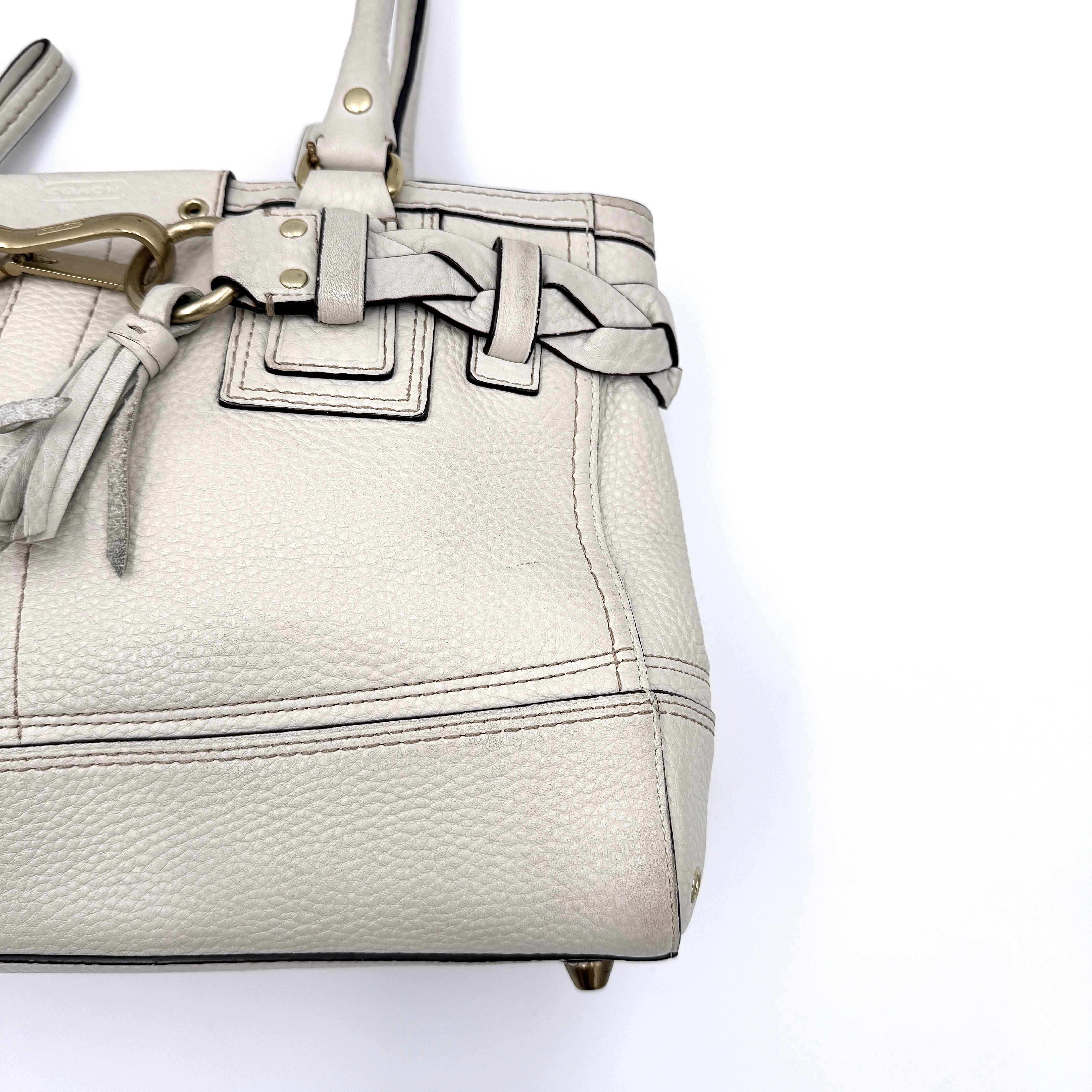 Coach Hampton Carryall in ivory leather with braided trim, brass dogleash clip, tassel, and top handles displayed against a white background.