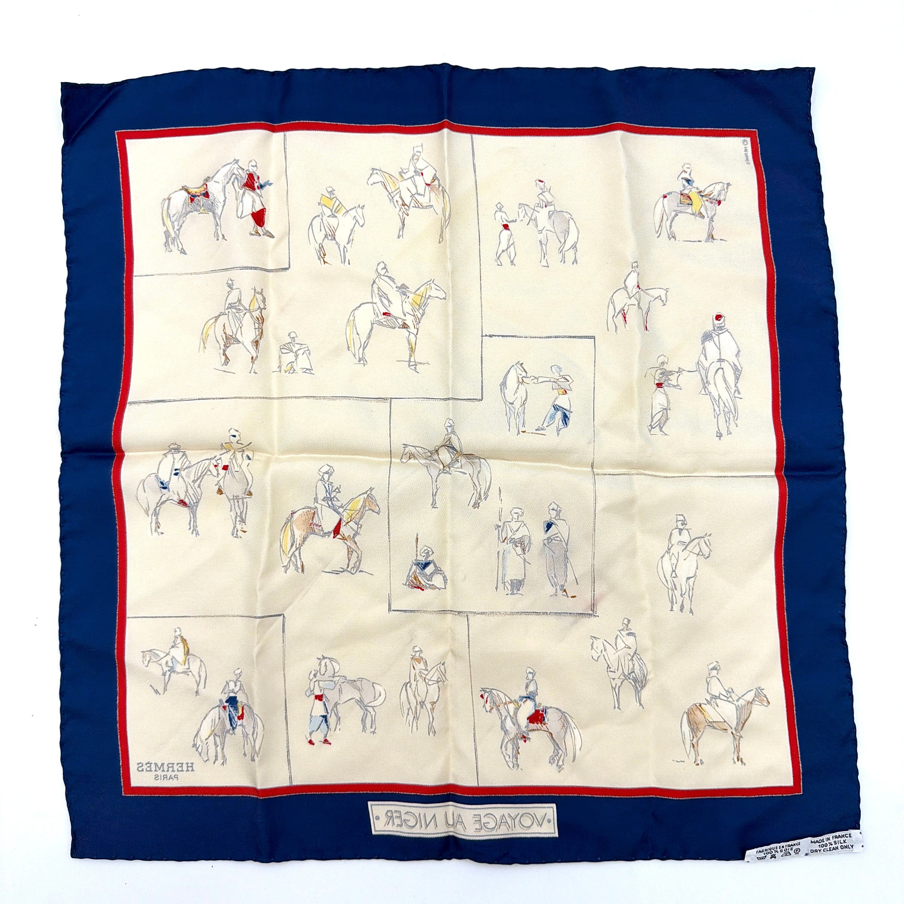 Hermès Voyage au Niger silk scarf in navy blue with cream center, featuring illustrative equestrian sketches bordered in red.