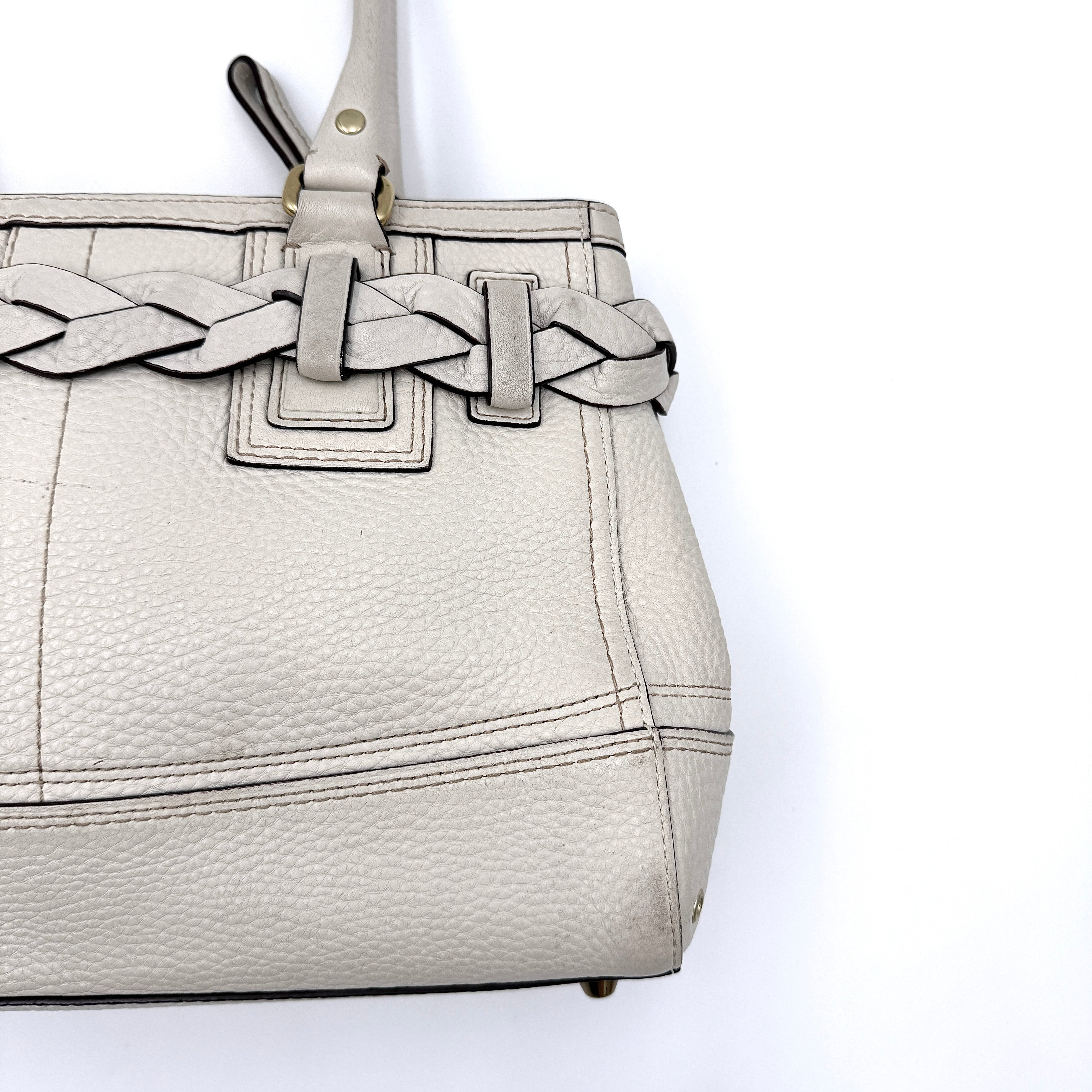 Coach Hampton Carryall in ivory leather with braided trim, brass dogleash clip, tassel, and top handles displayed against a white background.