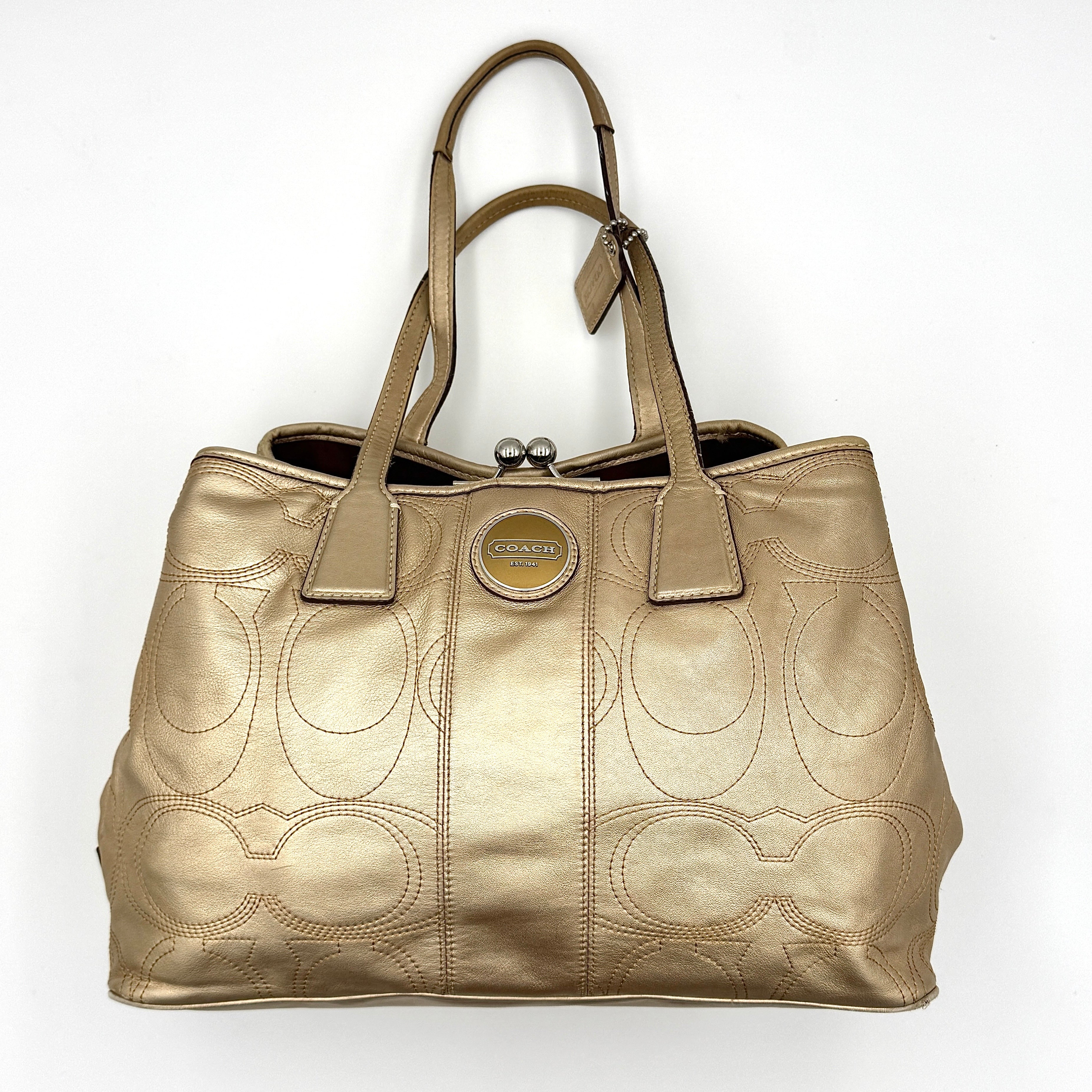 Coach metallic gold shoulder bag with signature embossed leather, double top handles, and a kisslock closure set against a clean background.