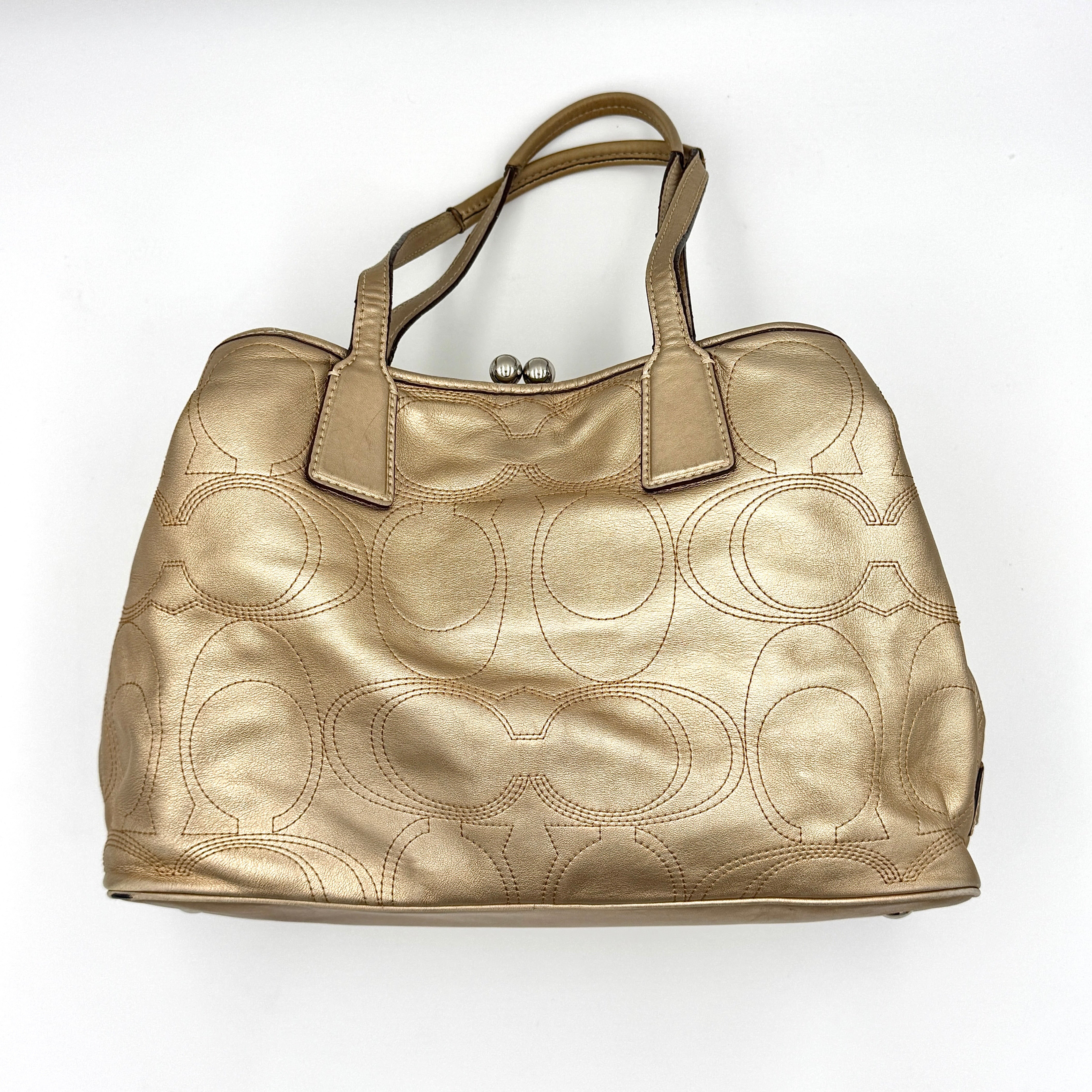 Coach metallic gold shoulder bag with signature embossed leather, double top handles, and a kisslock closure set against a clean background.