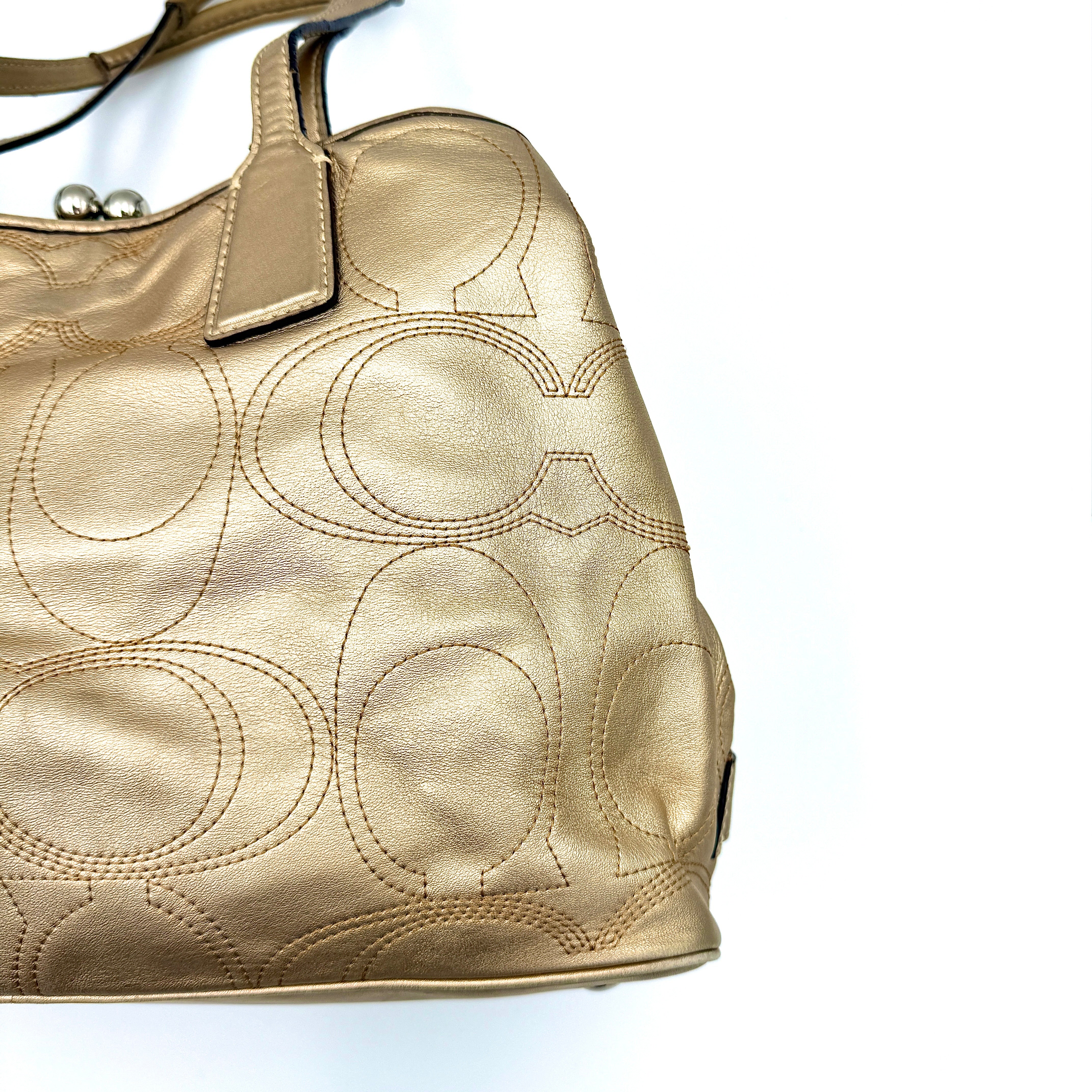 Coach metallic gold shoulder bag with signature embossed leather, double top handles, and a kisslock closure set against a clean background.